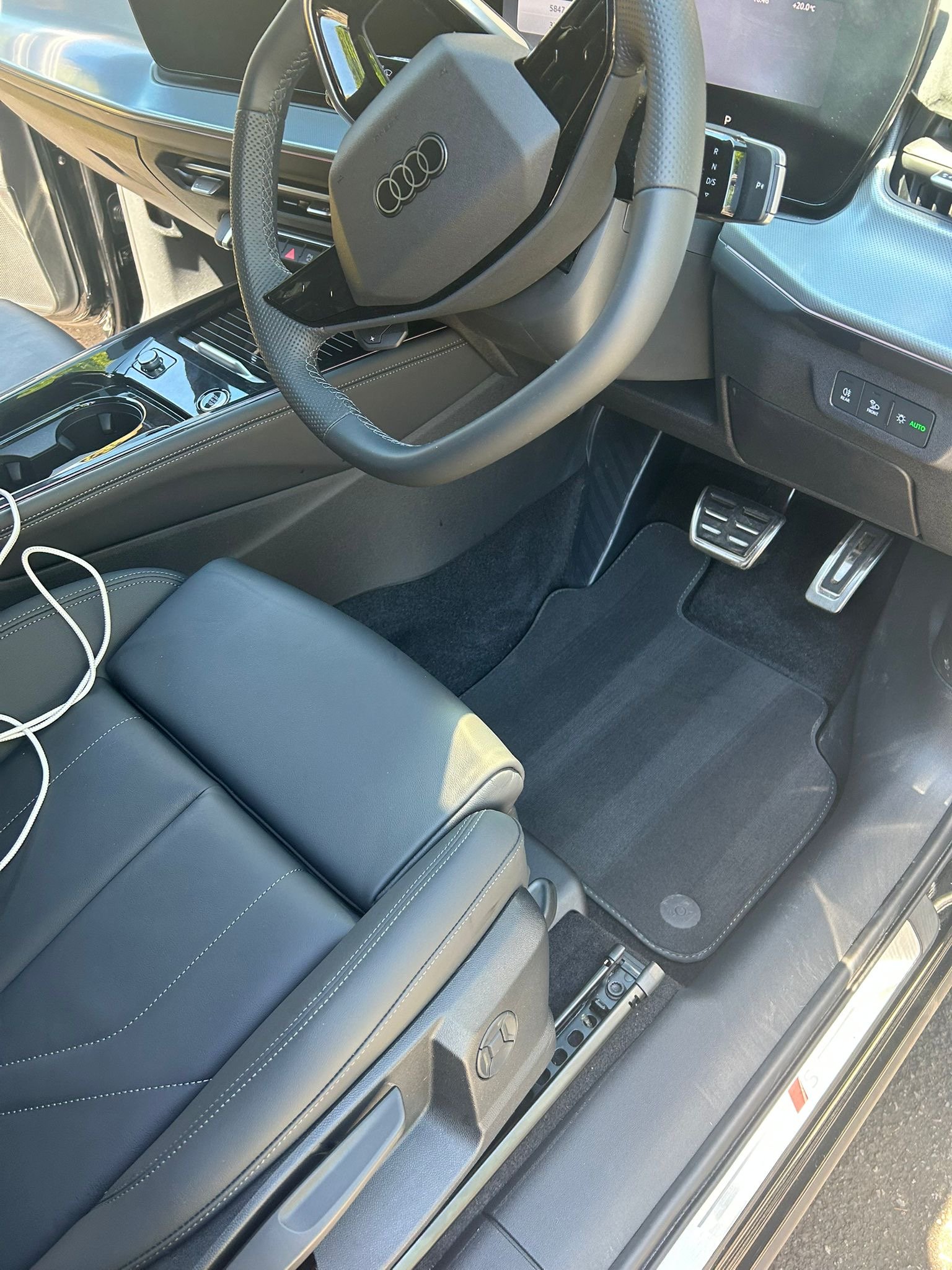 The interior of an Audi vehicle, featuring a steering wheel, digital dashboard, center console, and seat with white stitching.