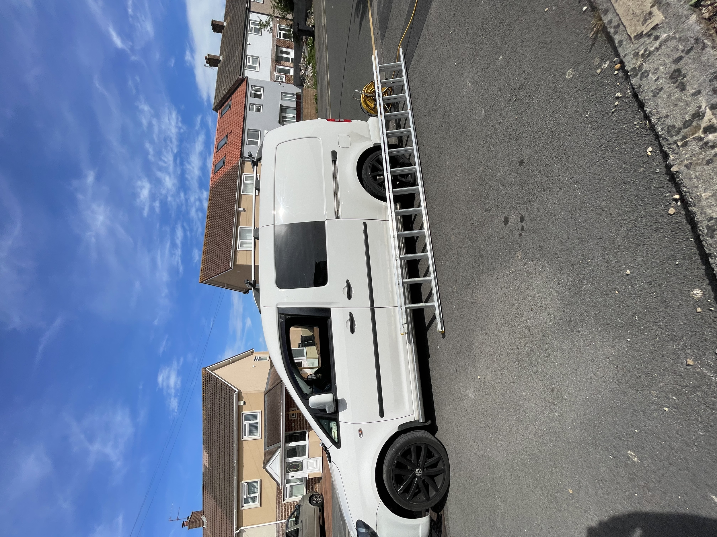 A white van with a ladder on top parked in a small parking lot.