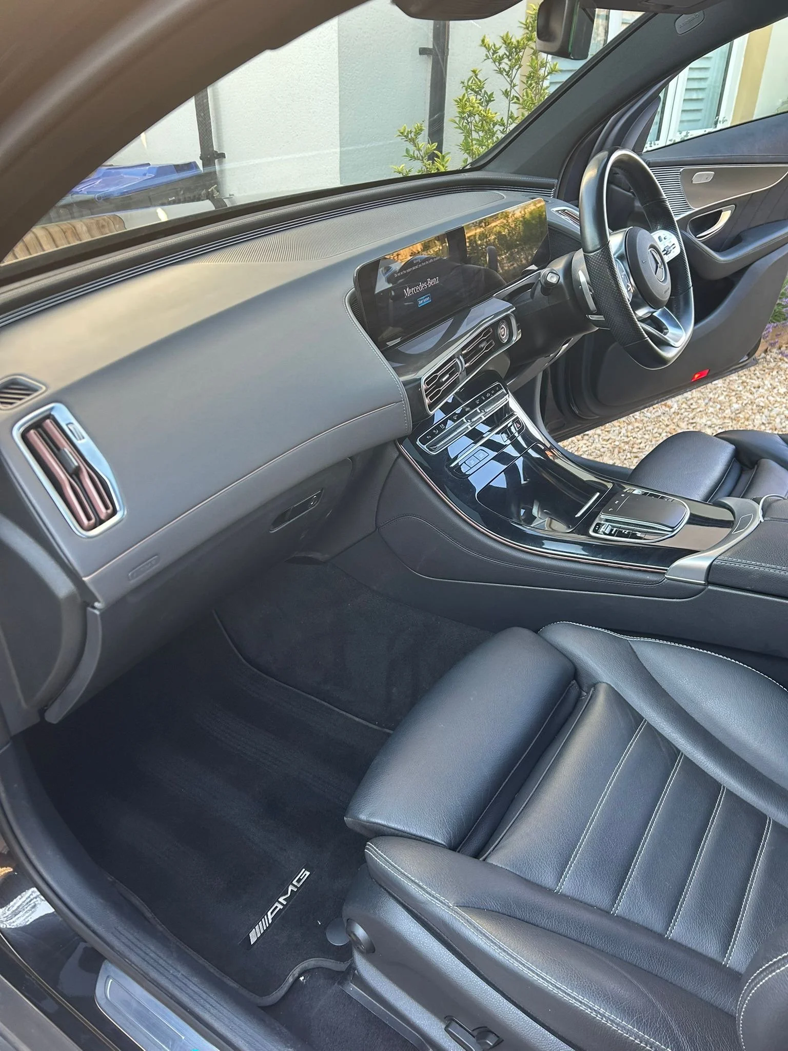Interior of a black Mercedes-Benz car with black leather seats, a digital dashboard display, and an AMG branded floor mat.