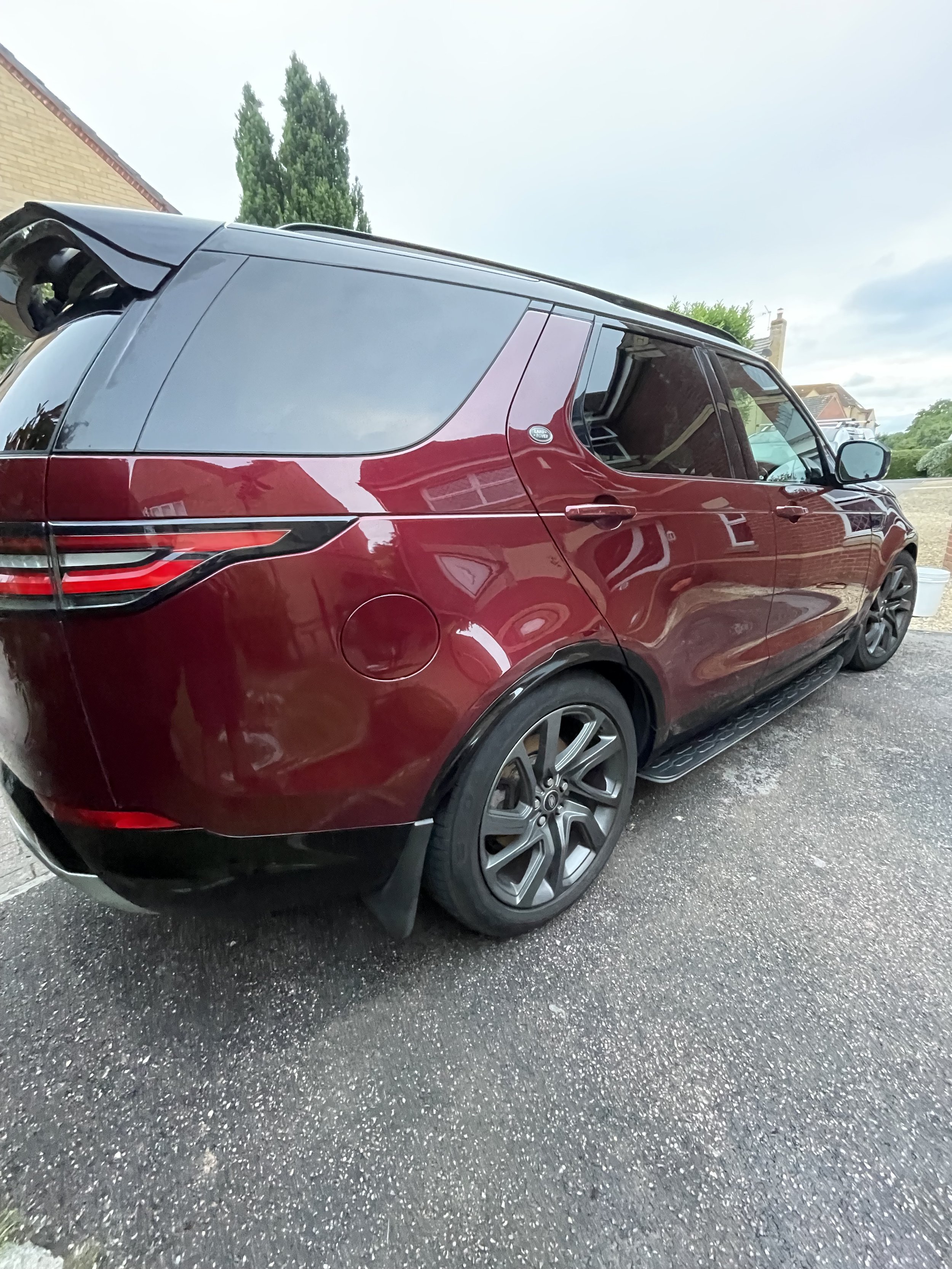 A red SUV parked on a driveway with a brick house and greenery in the background.