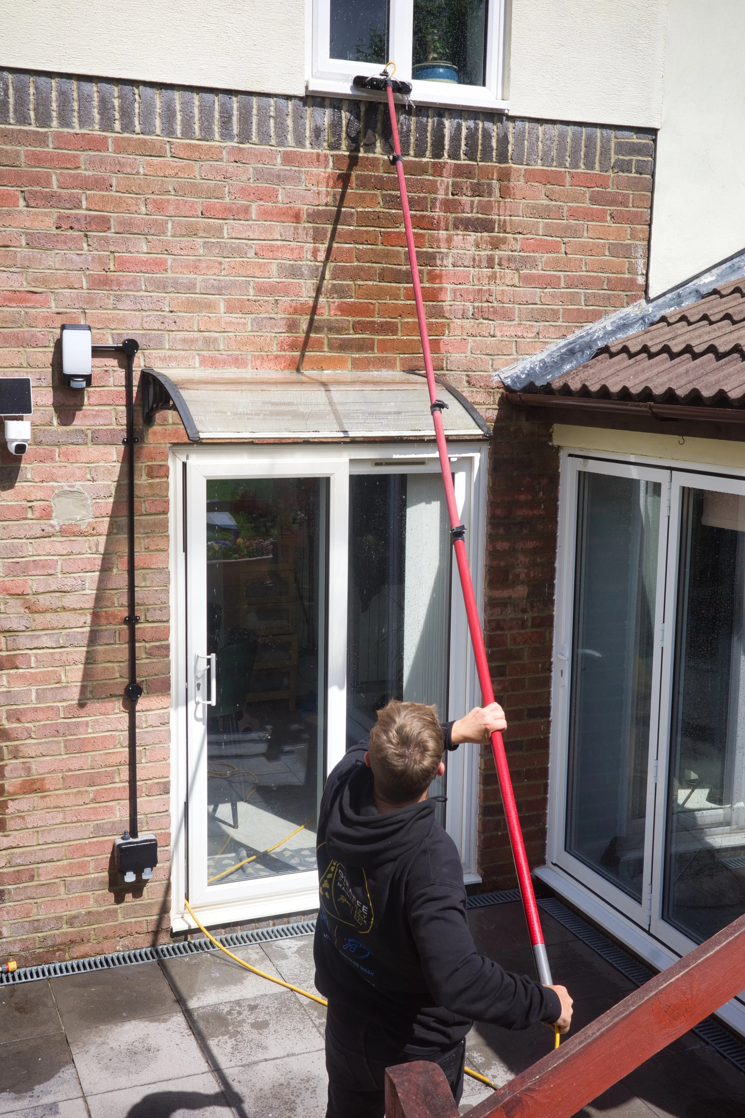 A person using a long pole to clean a glass door outside a house.