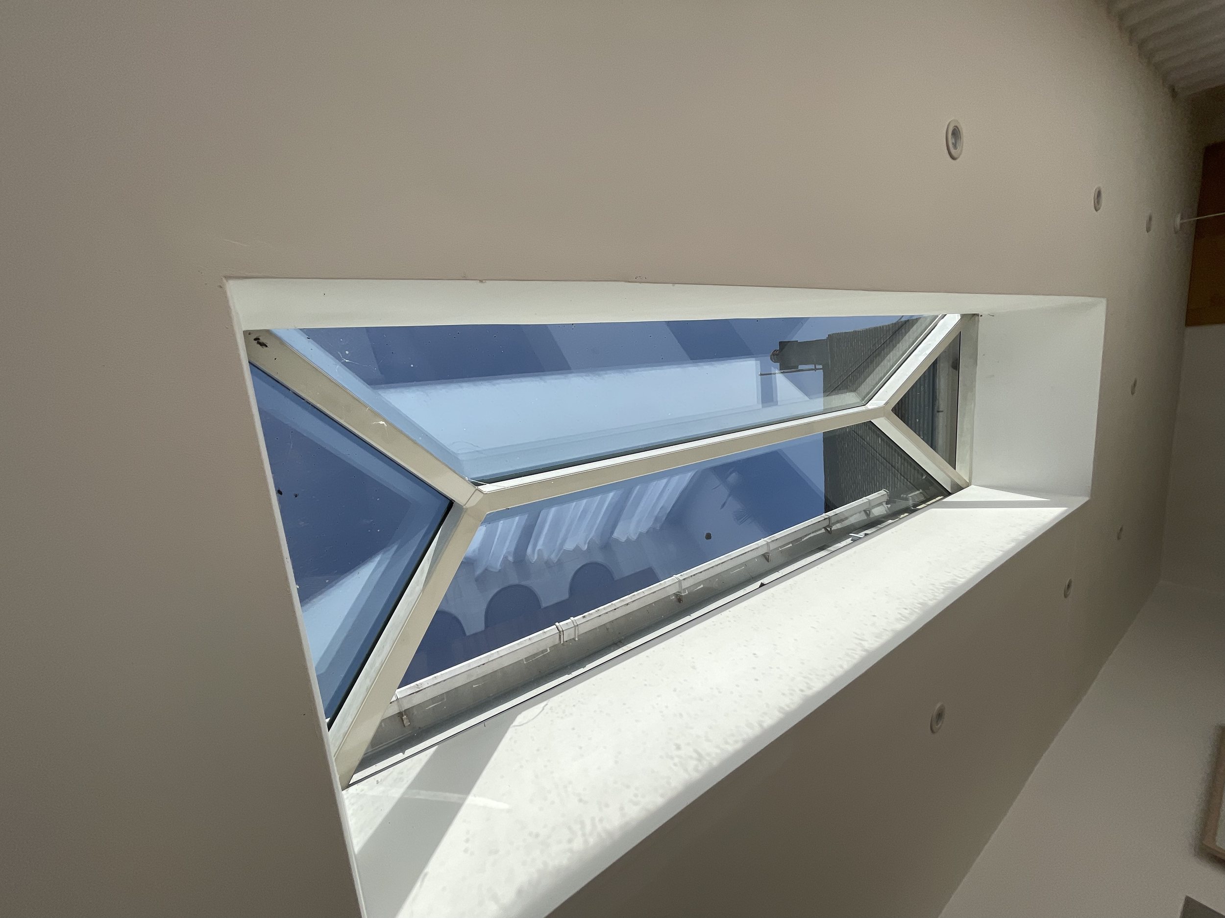 A white windowsill with a large open window showing a clear blue sky and a railing outside.