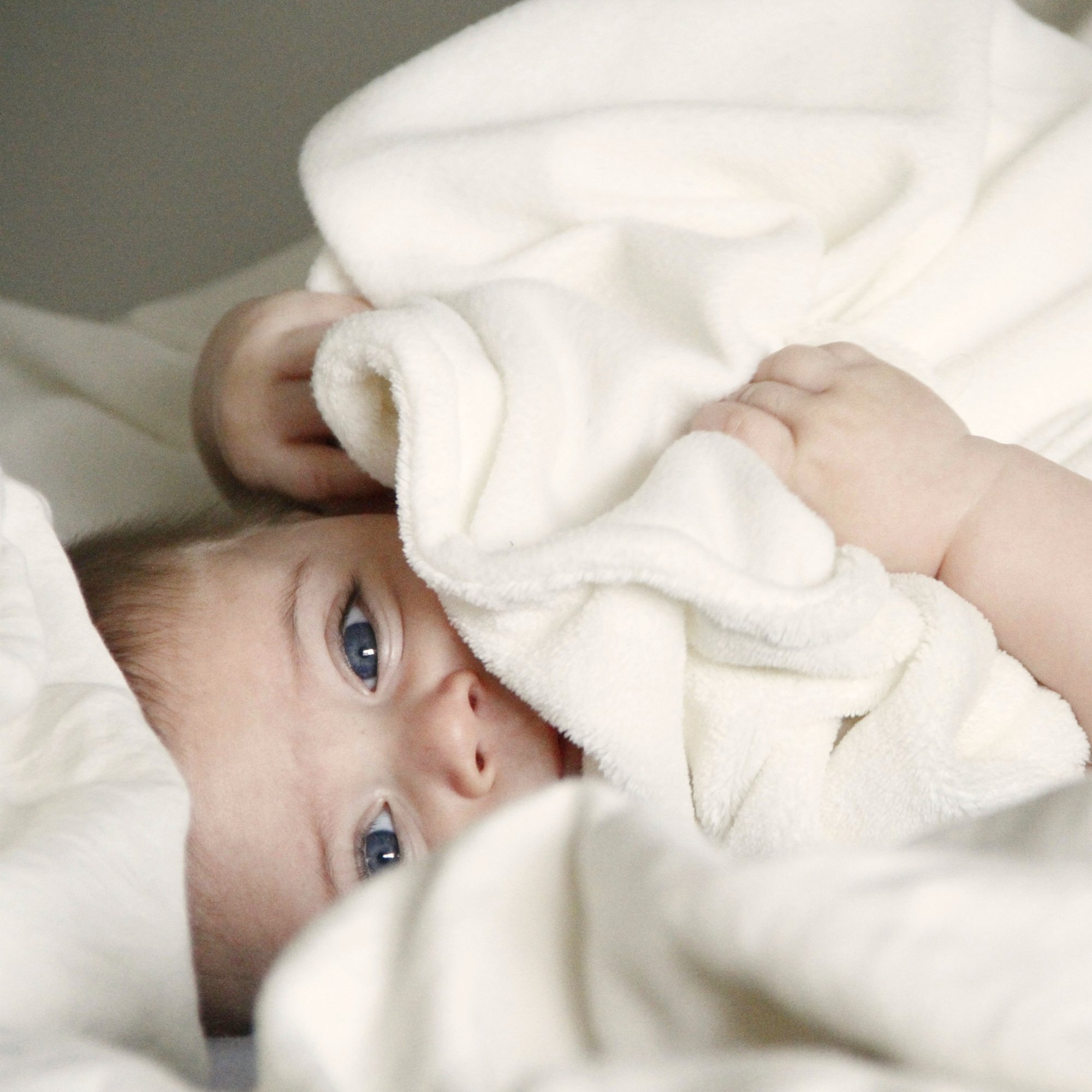 Baby unter einer hellen Decke im Abschnitt über mögliche Anliegen in der Kinderosteopathie.