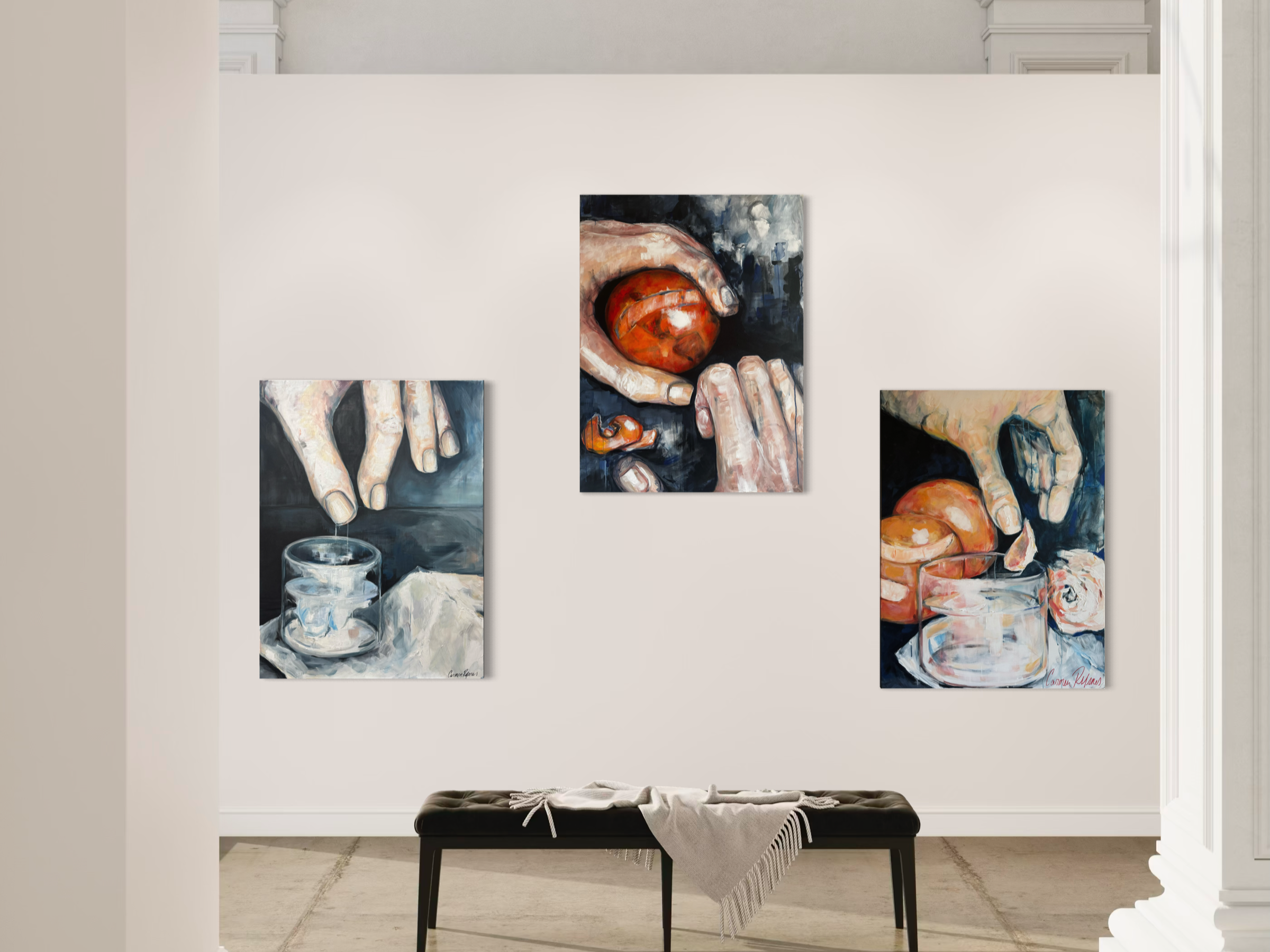 Three paintings of hands holding peaches are displayed on a plain white wall in an art gallery. A black bench with a beige cloth is placed below the paintings.