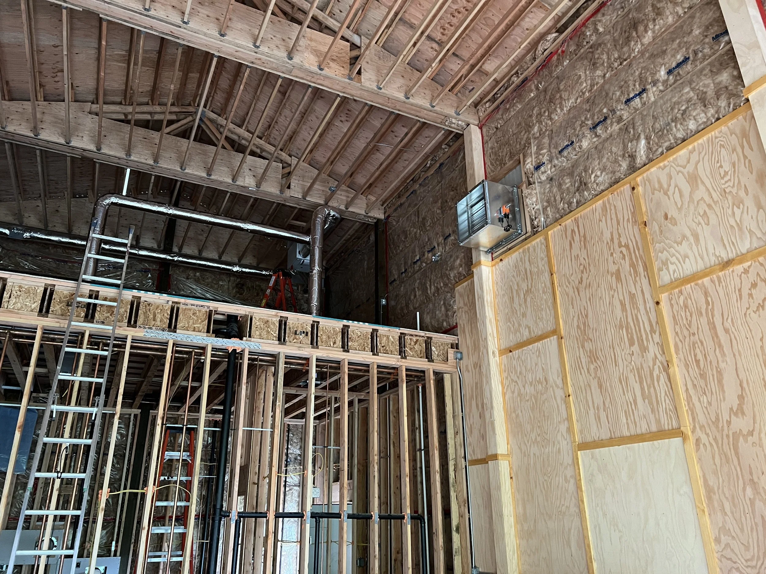 Interior of a building under construction with wooden framing, ductwork, and partial wall sheathing.