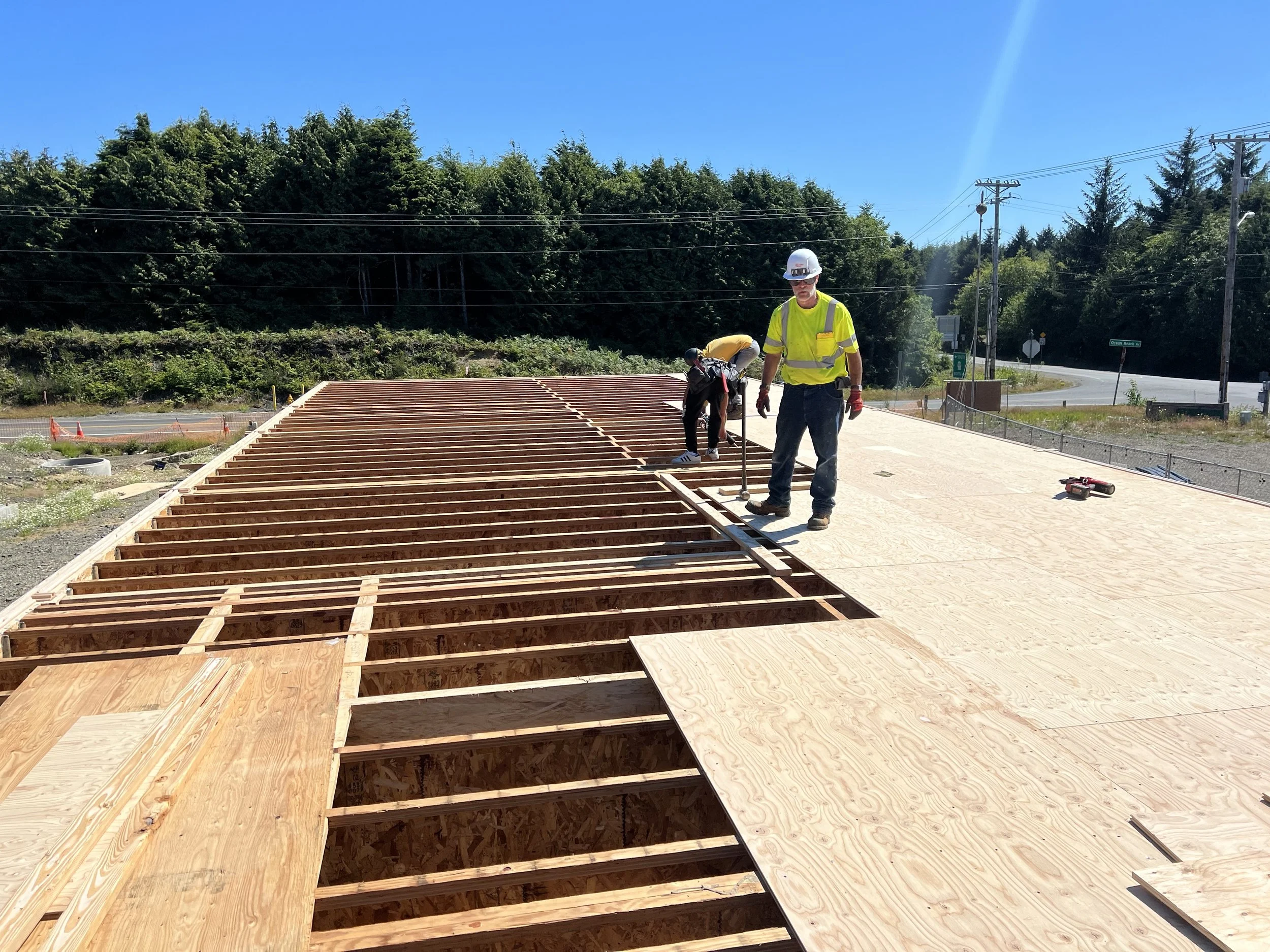 Construction workers building a wooden deck beside a street, with trees and utility poles in the background.