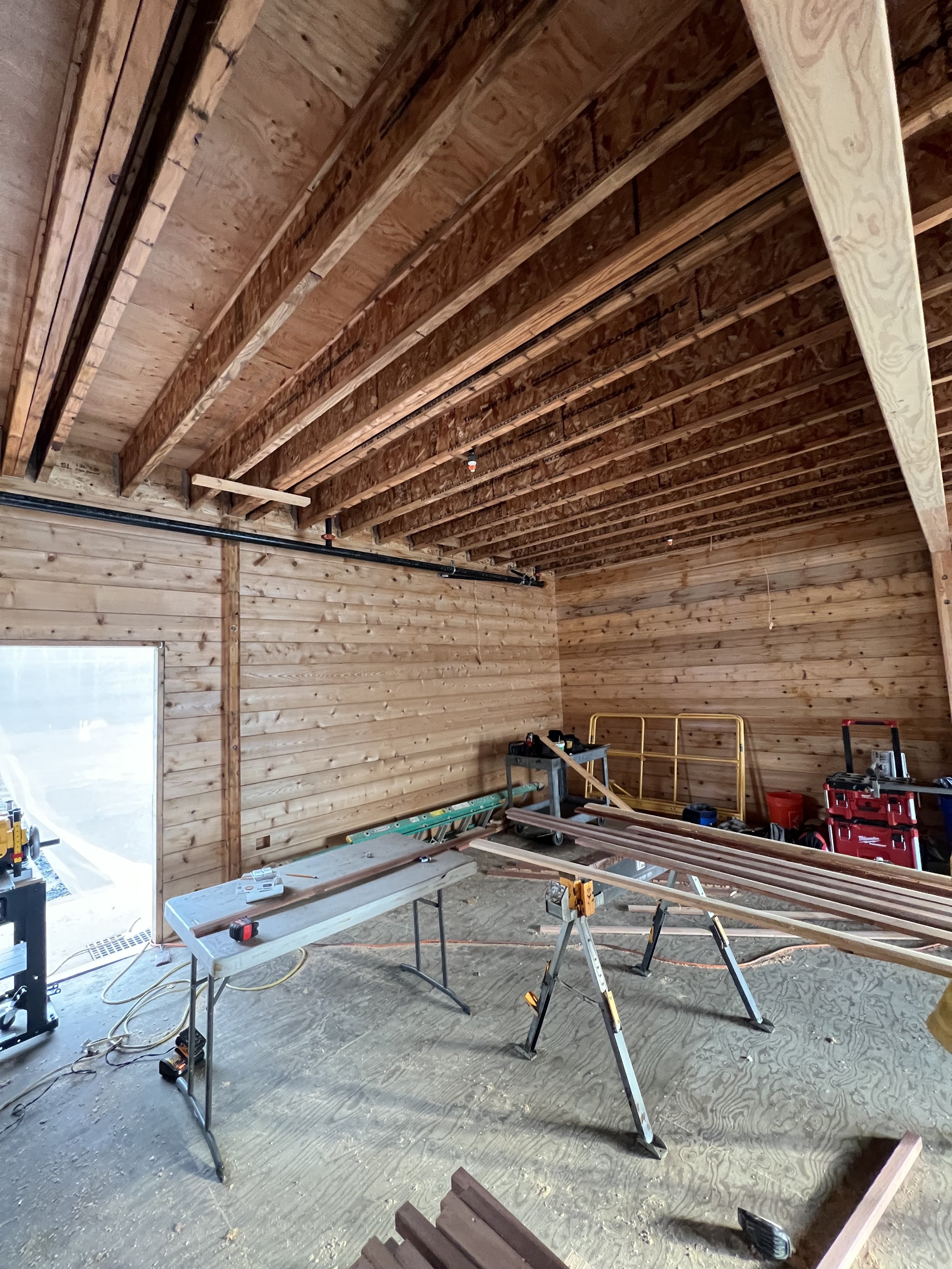 Construction site inside a building under renovation, with exposed wooden ceiling beams, construction tools, and equipment on the floor.