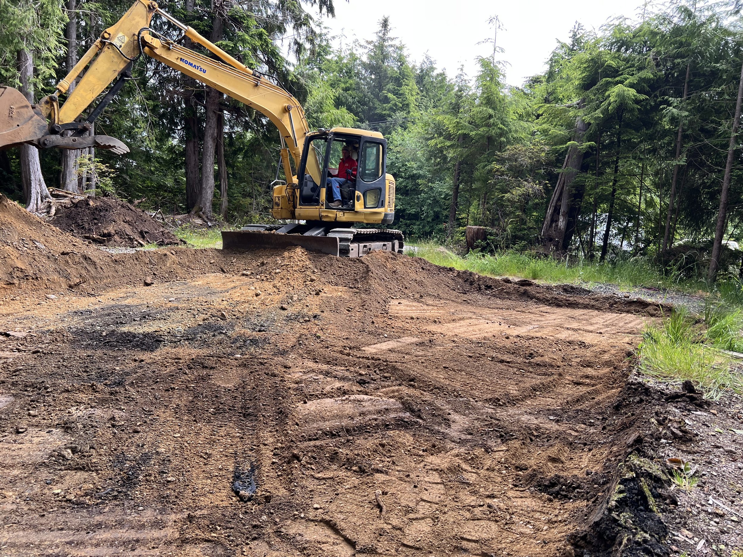 A yellow excavation excavator moving dirt on a construction site in a forested area.