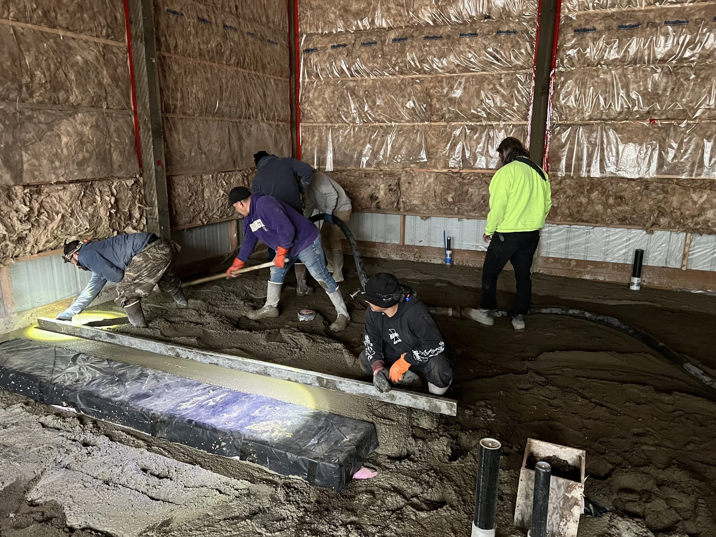Construction workers pouring and leveling concrete in a building's foundation or basement.