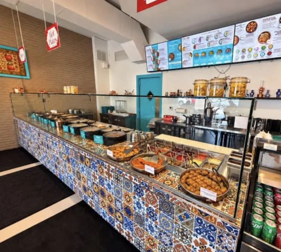 Colorful Turkish tile counter with trays of hot food and menu screens at Clay Pot in Naples