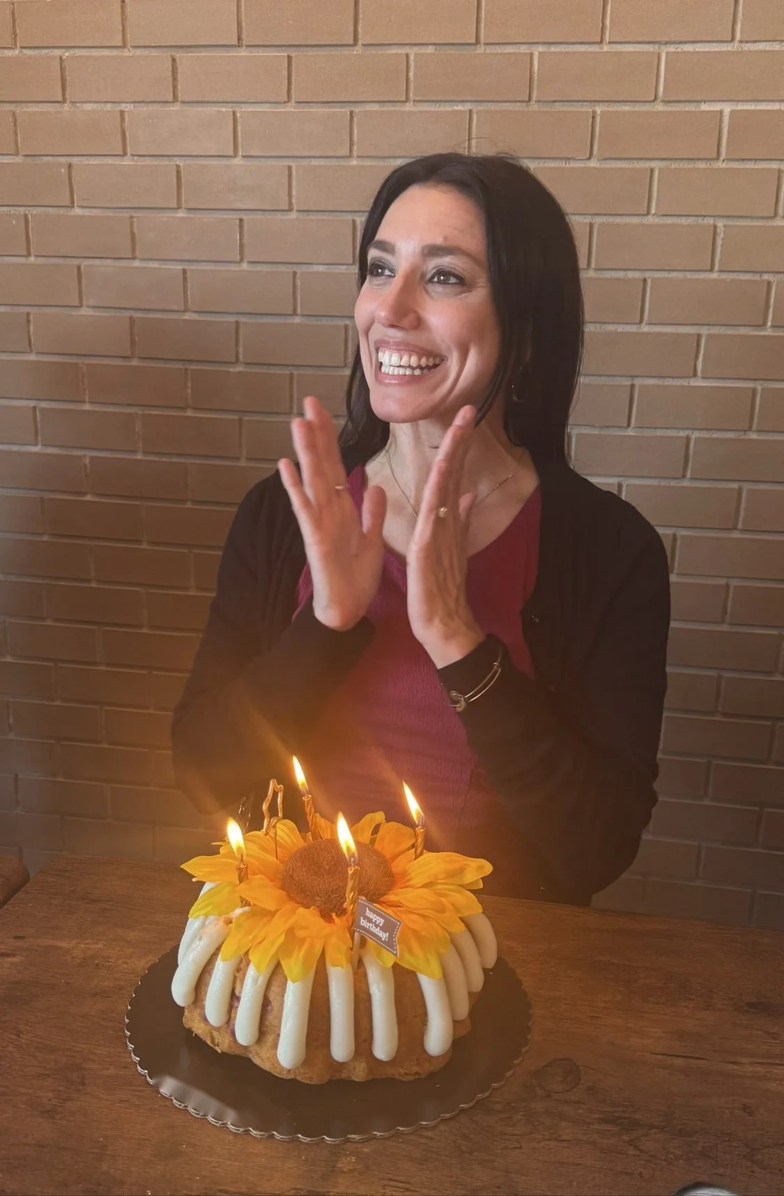 Birthday cake with lit candles and a delighted guest clapping at Clay Pot in Naples