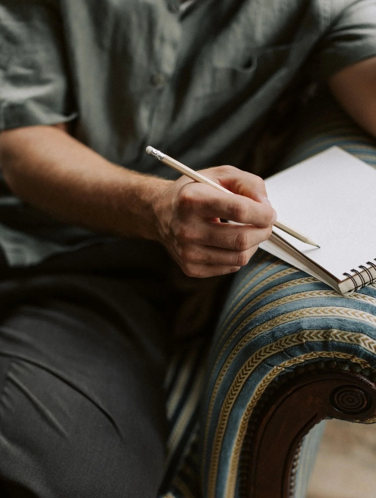 A person holding a lined notepad and a pencil, sitting on a colorful, striped upholstered chair.
