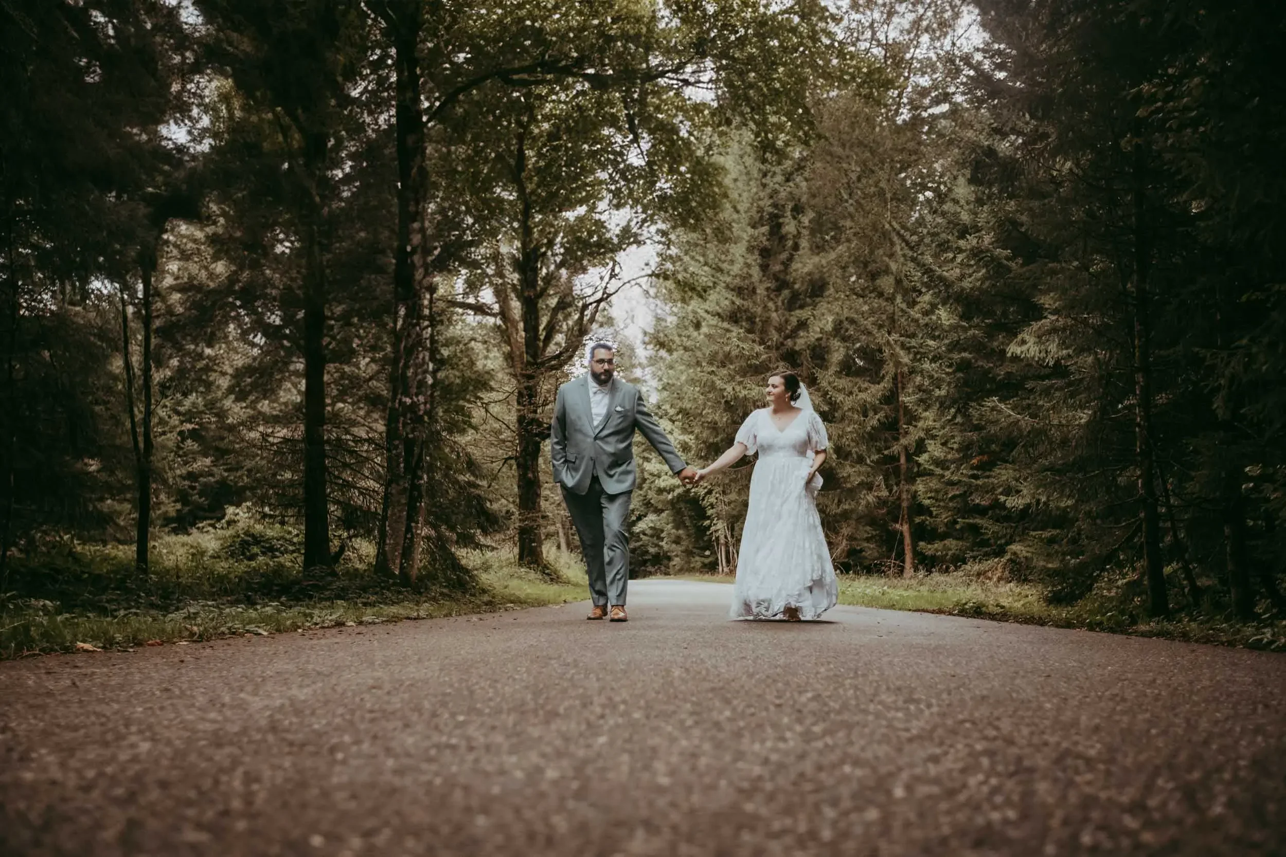 Ein Paar in Hochzeitskleidung läuft Hand in Hand durch einen Wald.