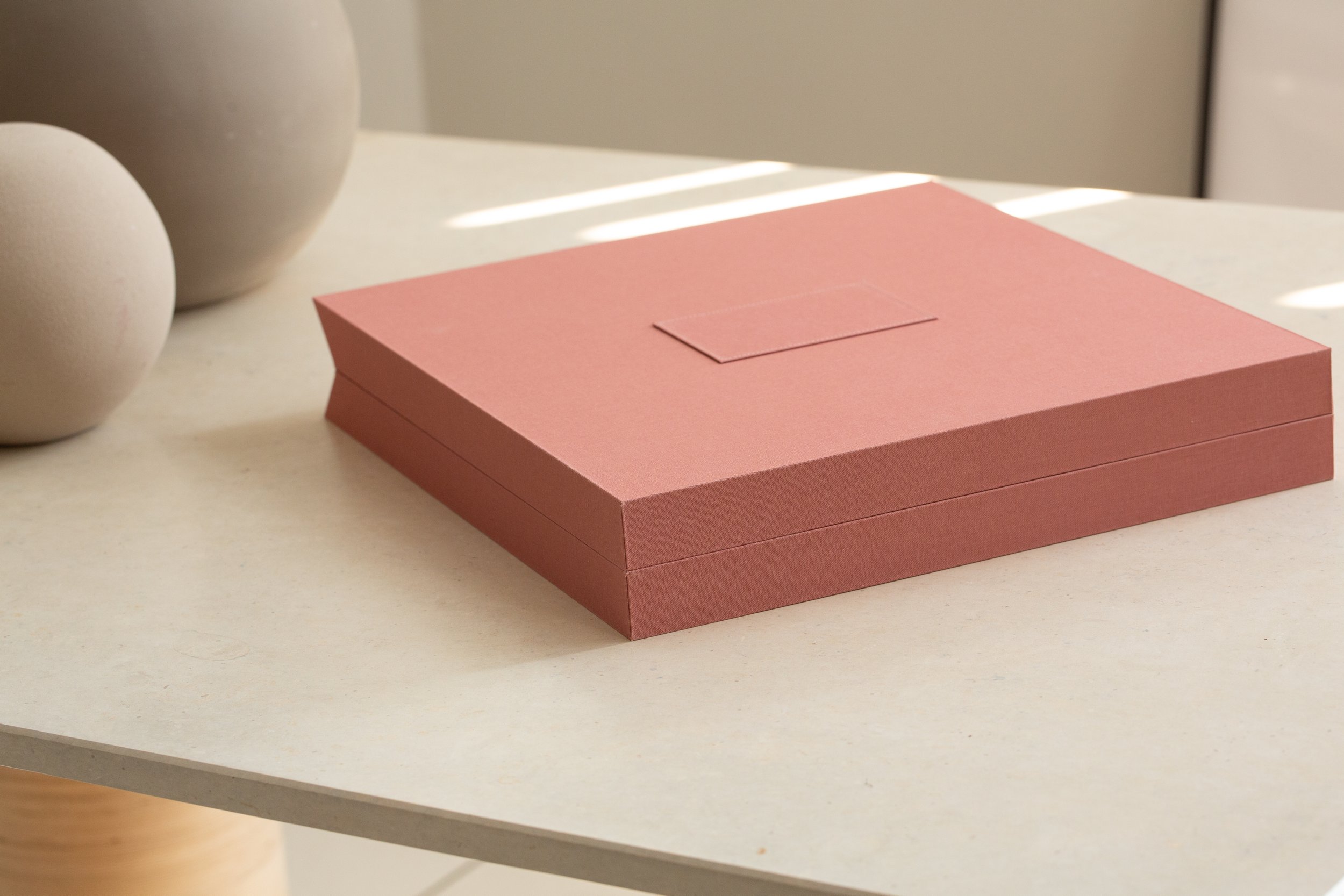 Ein rosa Schmuckkästchen mit Deckel auf einem weißen Tisch, im Hintergrund weiße Keramikvasen, Lichtreflexionen auf der Tischoberfläche.