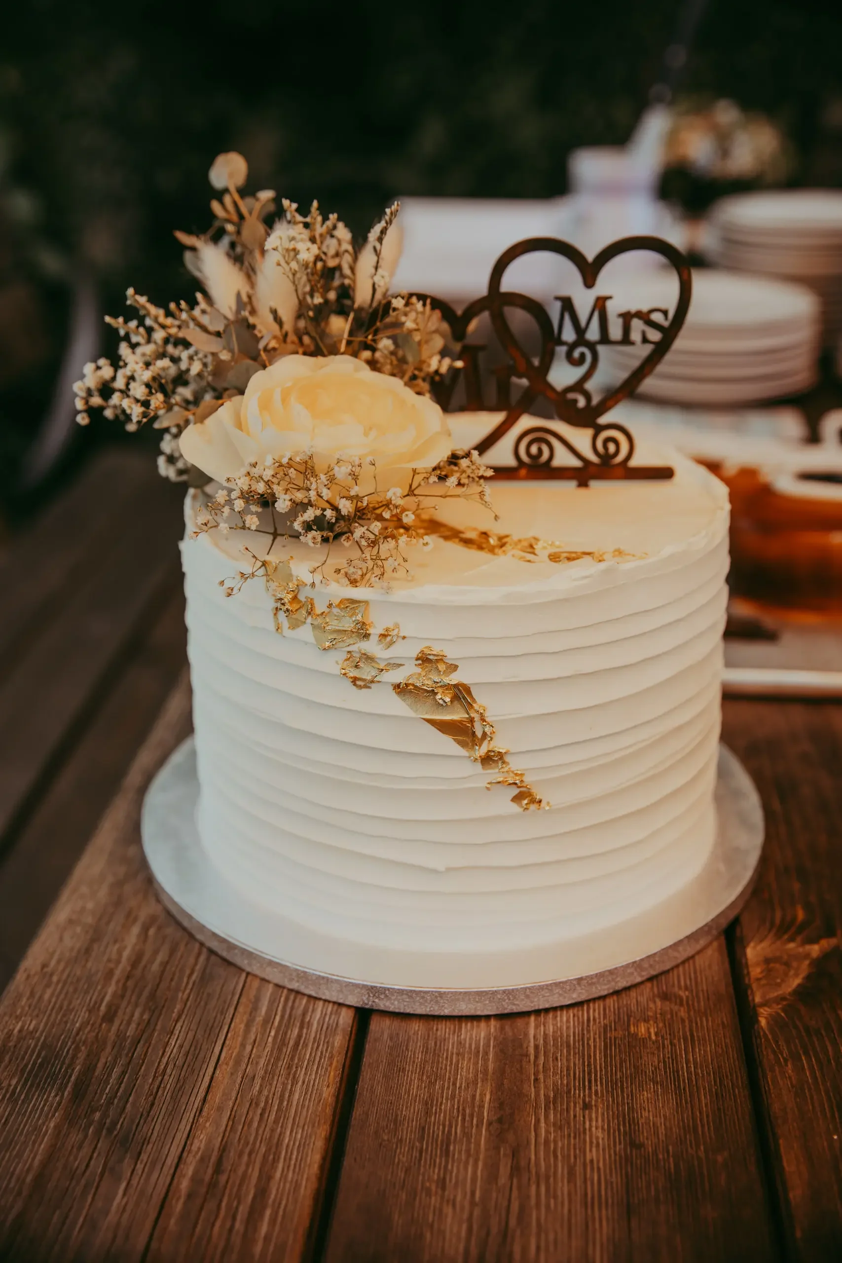 Weiße Hochzeitstorte mit Kerzen, Blumen und einem 'Mrs' Dekor auf einem rustikalen Holztisch.