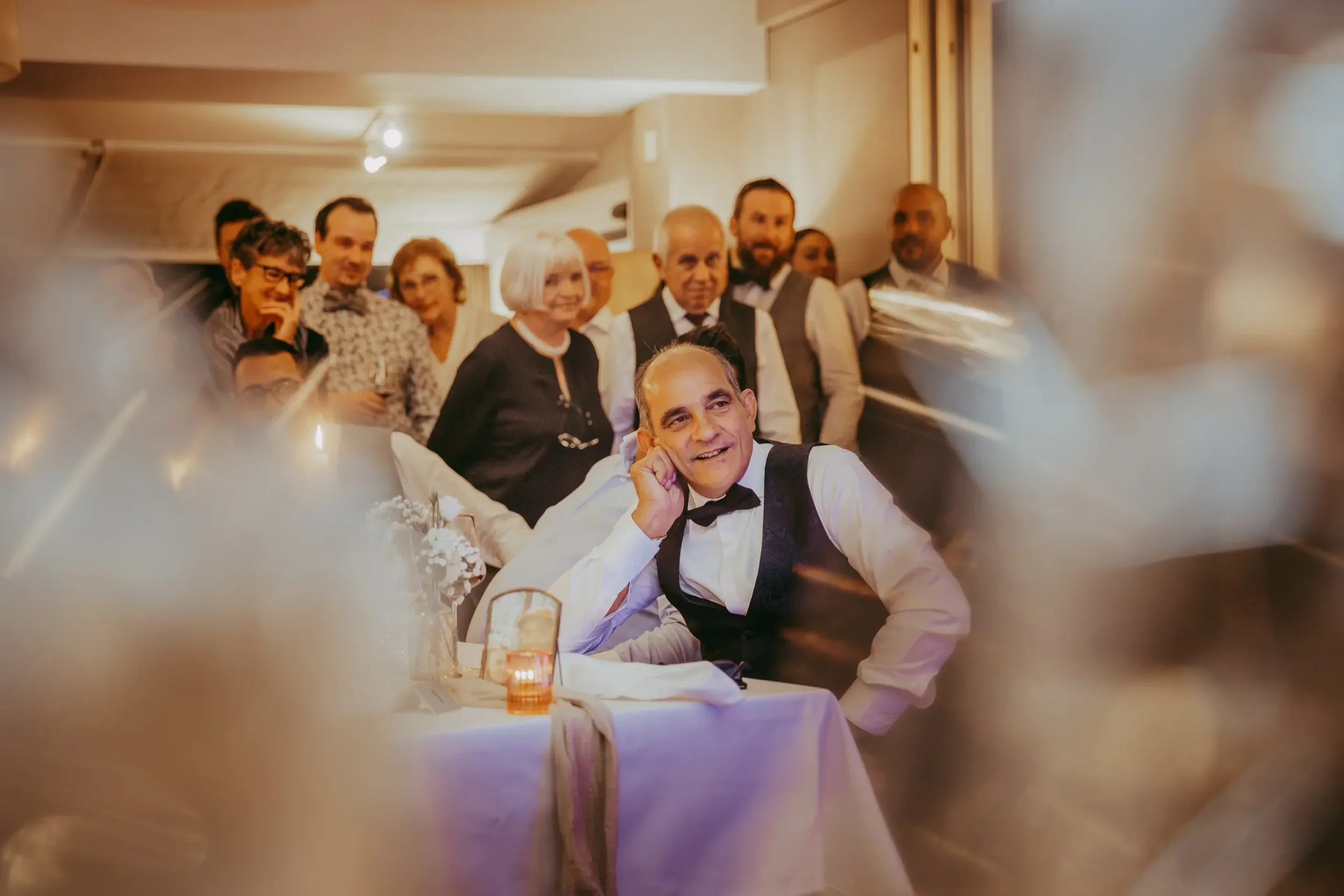 Gruppe von Menschen bei einem Fest, sitzend an einem Tisch mit Kerzen, Stimmung ist festlich.