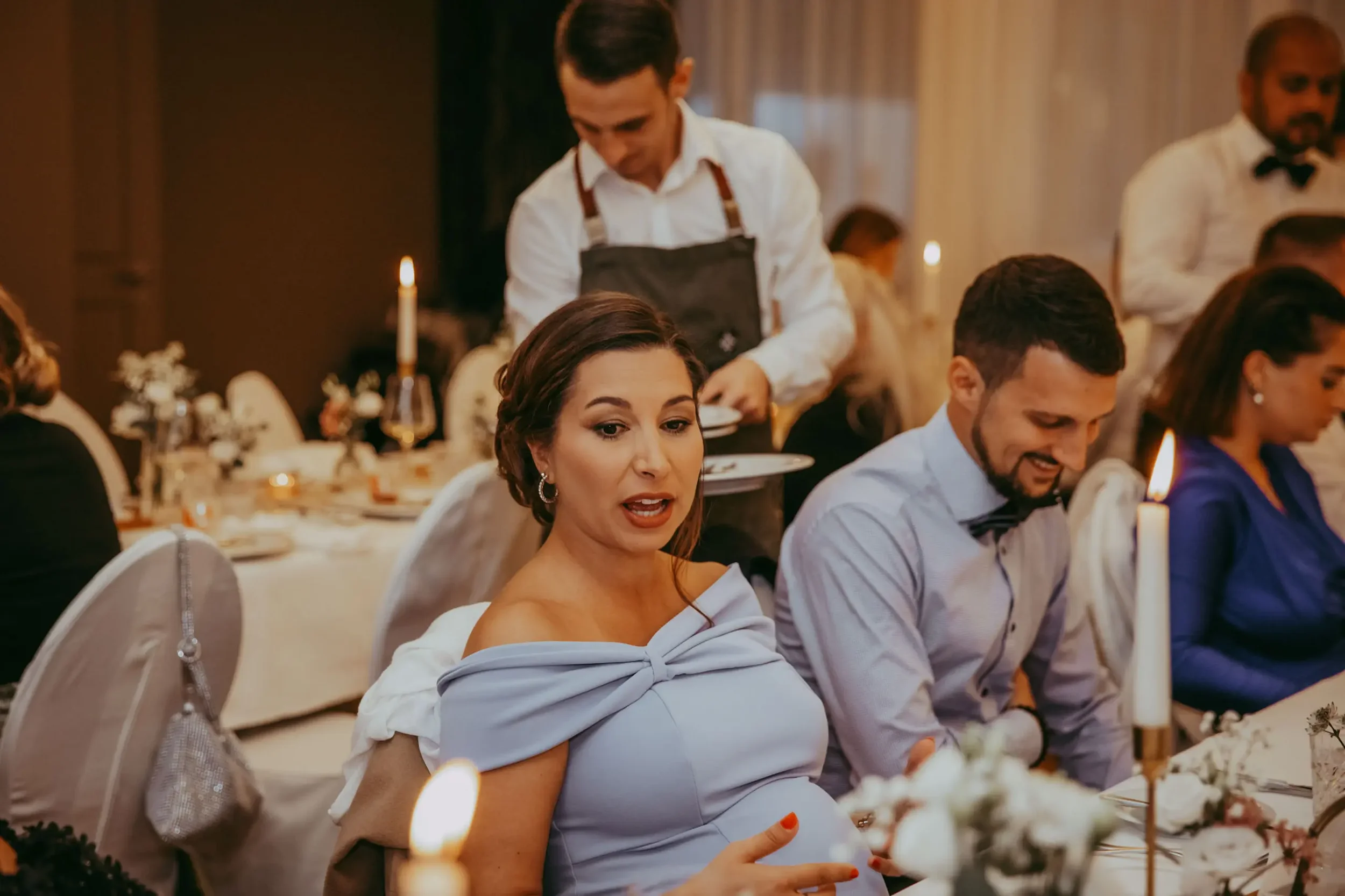 Menschen bei einer eleganten Dinnerveranstaltung, einige tragen formelle Kleidung und Fliegen, in einem festlich dekorierten Raum mit Kerzen.