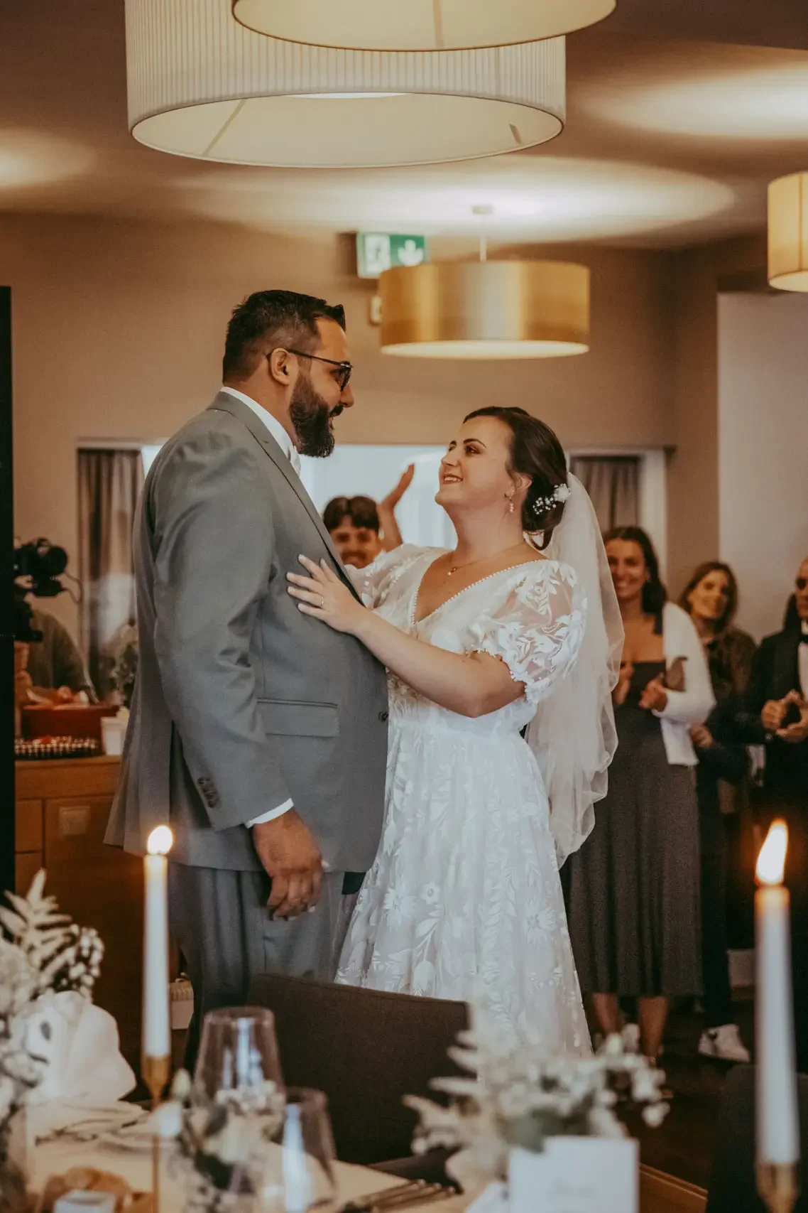 Ein Brautpaar tanzt bei einer Hochzeit im festlichen Raum, umgeben von lachenden Gästen.