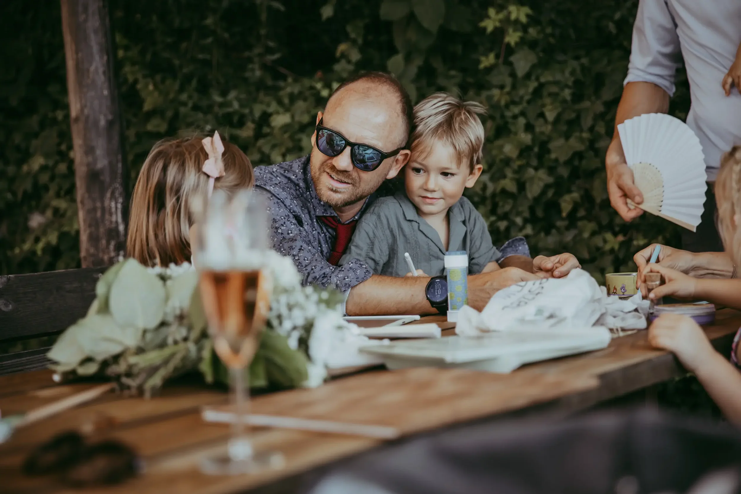 Familie beim Essen im Freien während eines Treffens im Grünen, mit Blumen und Pflanzen im Hintergrund.