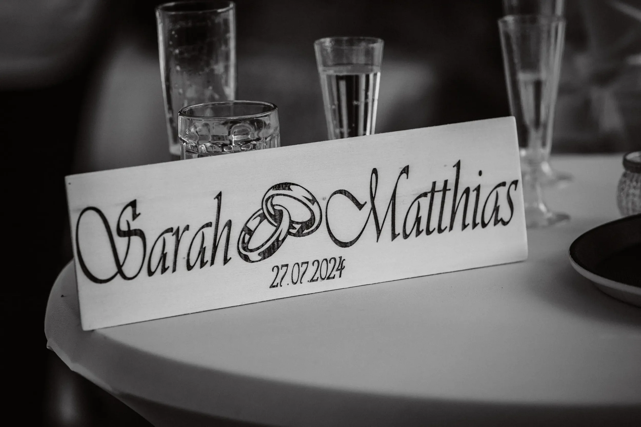 Tisch mit Gläsern und einer Karte, die für eine Hochzeit am 27.07.2024 am Meer steht.