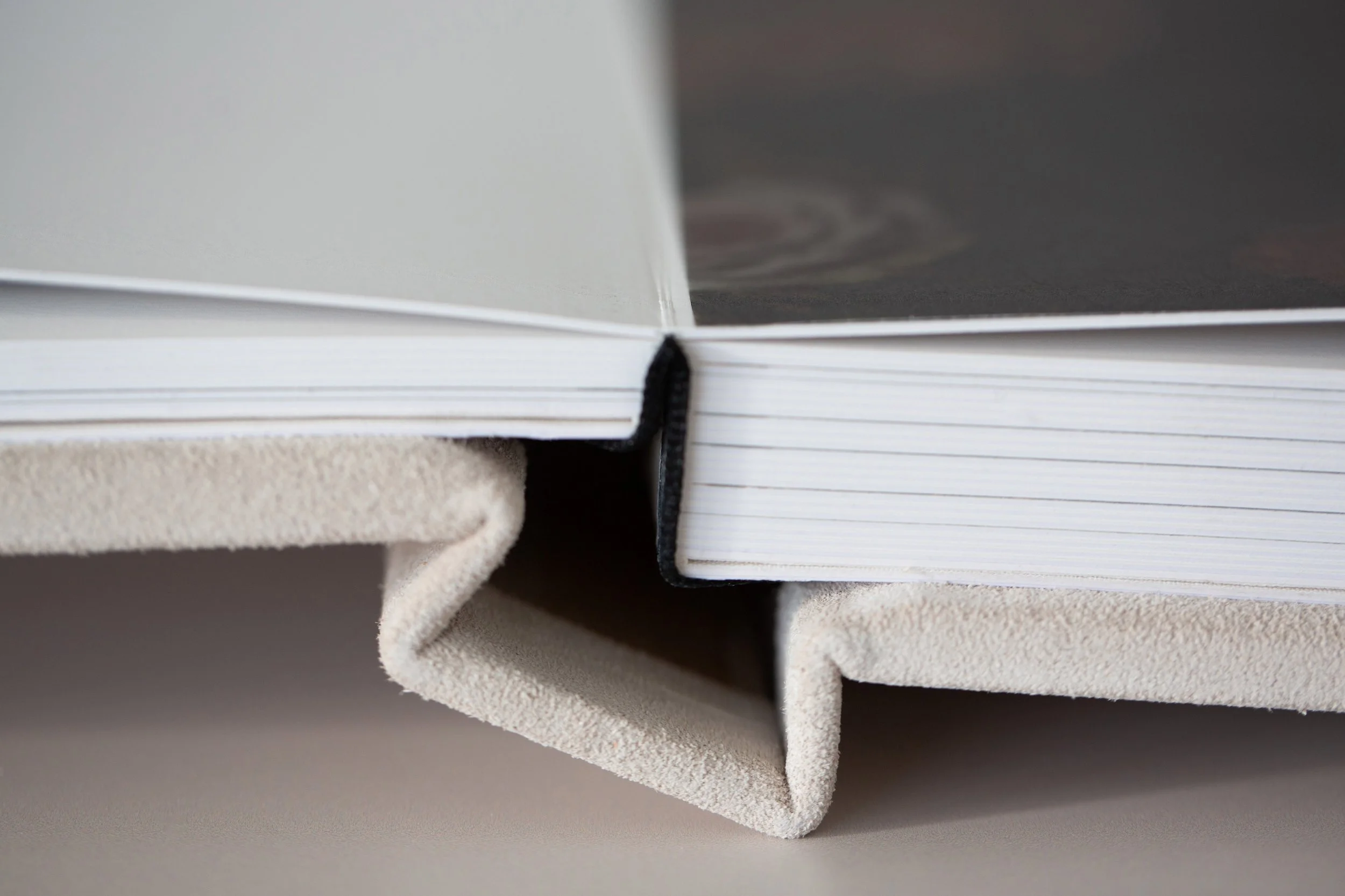 Buch mit offener schwarzer und weißer Seite auf grauem Hintergrund, mit Lesezeichen. Das Buch liegt auf einem beigen, weichen Stoff. 