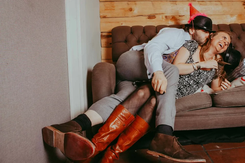 Ein Paar posiert lachend und ausgelassen auf einem Sofa vor der Fotobox