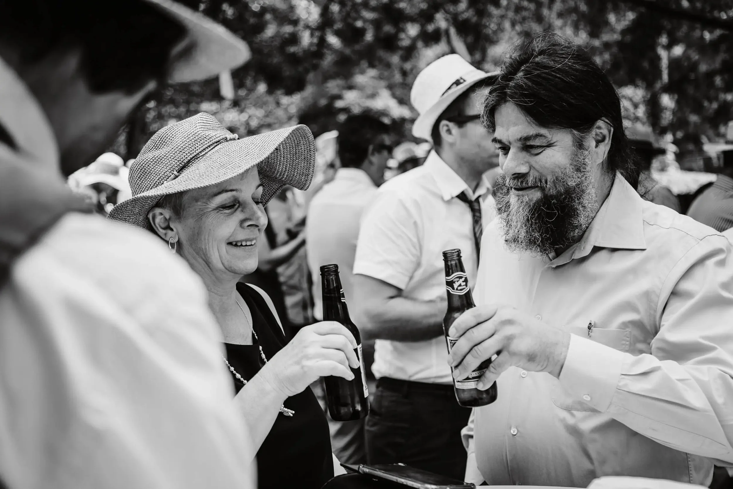 Menschen beim Trinken und Gespräch auf einer Feier, im Vordergrund eine Frau und ein Mann, beide halten Bierflaschen, im Hintergrund weitere Personen.