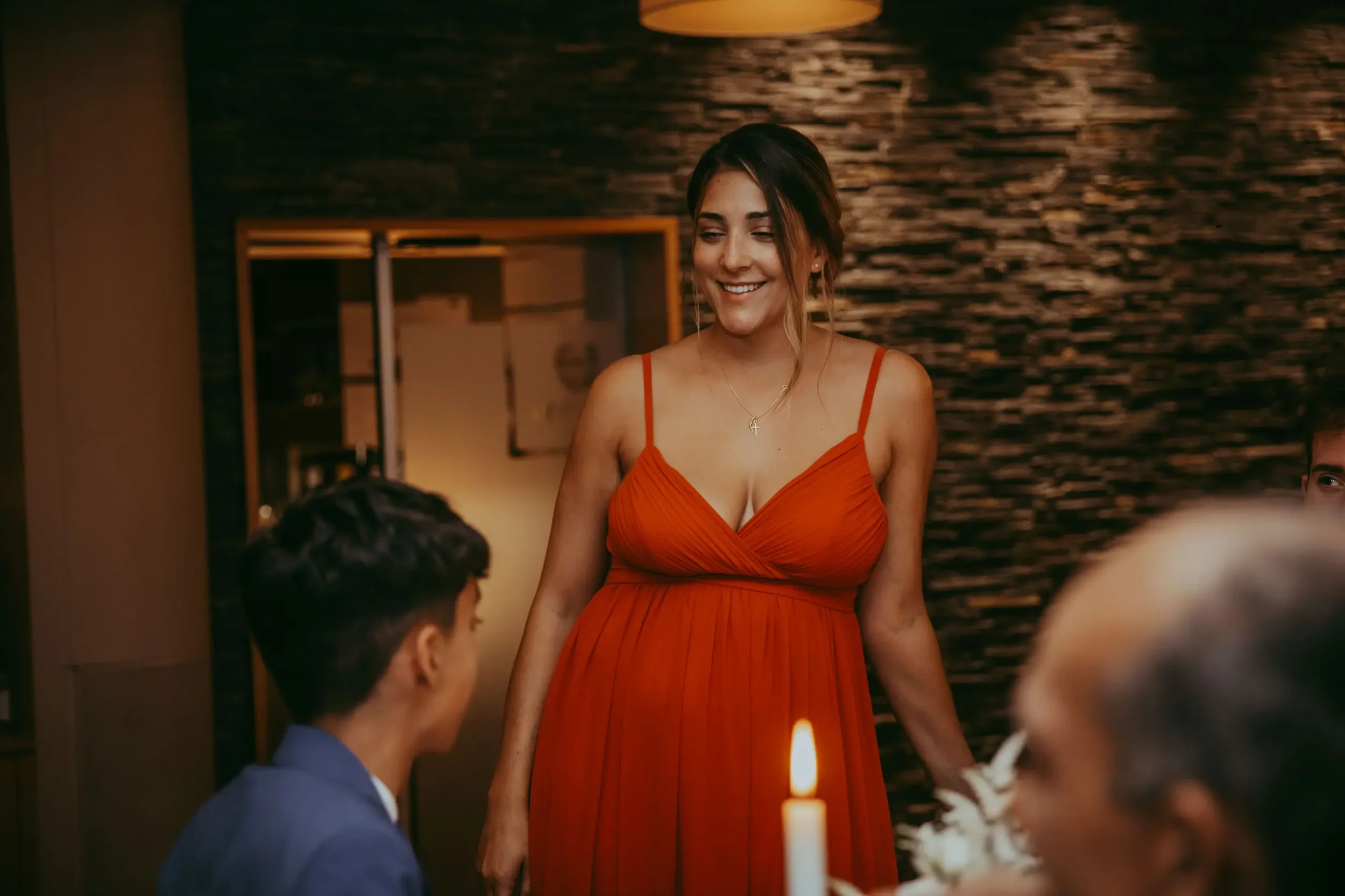 Eine Frau trägt ein rotes Kleid und lächelt beim Abendessen in einem Restaurant mit dunklem Steingartenhintergrund.