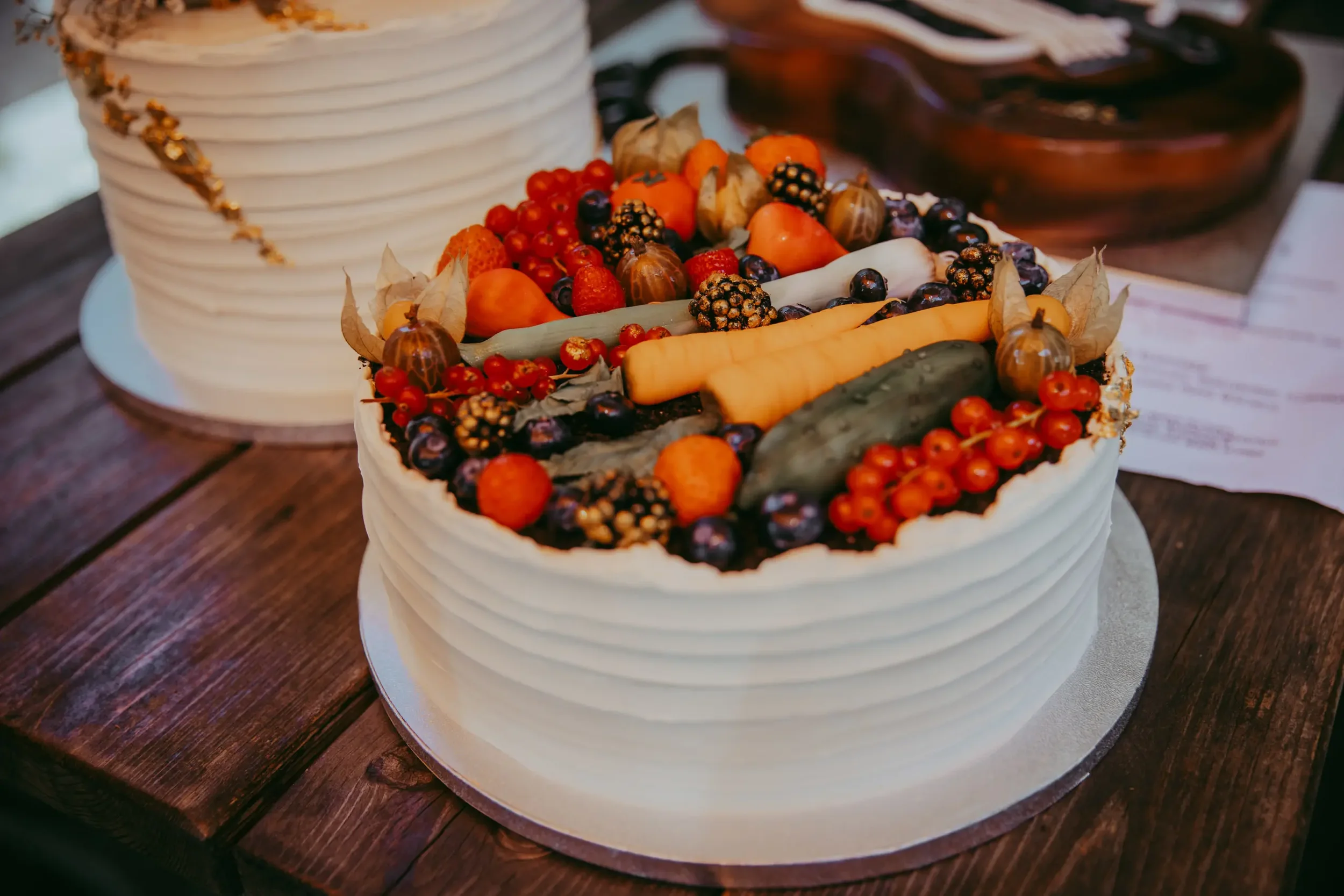 Obsttorte mit buntem Obst und Beeren, umgeben von einem weißen Baiser-Rand, auf einem Holztablett.