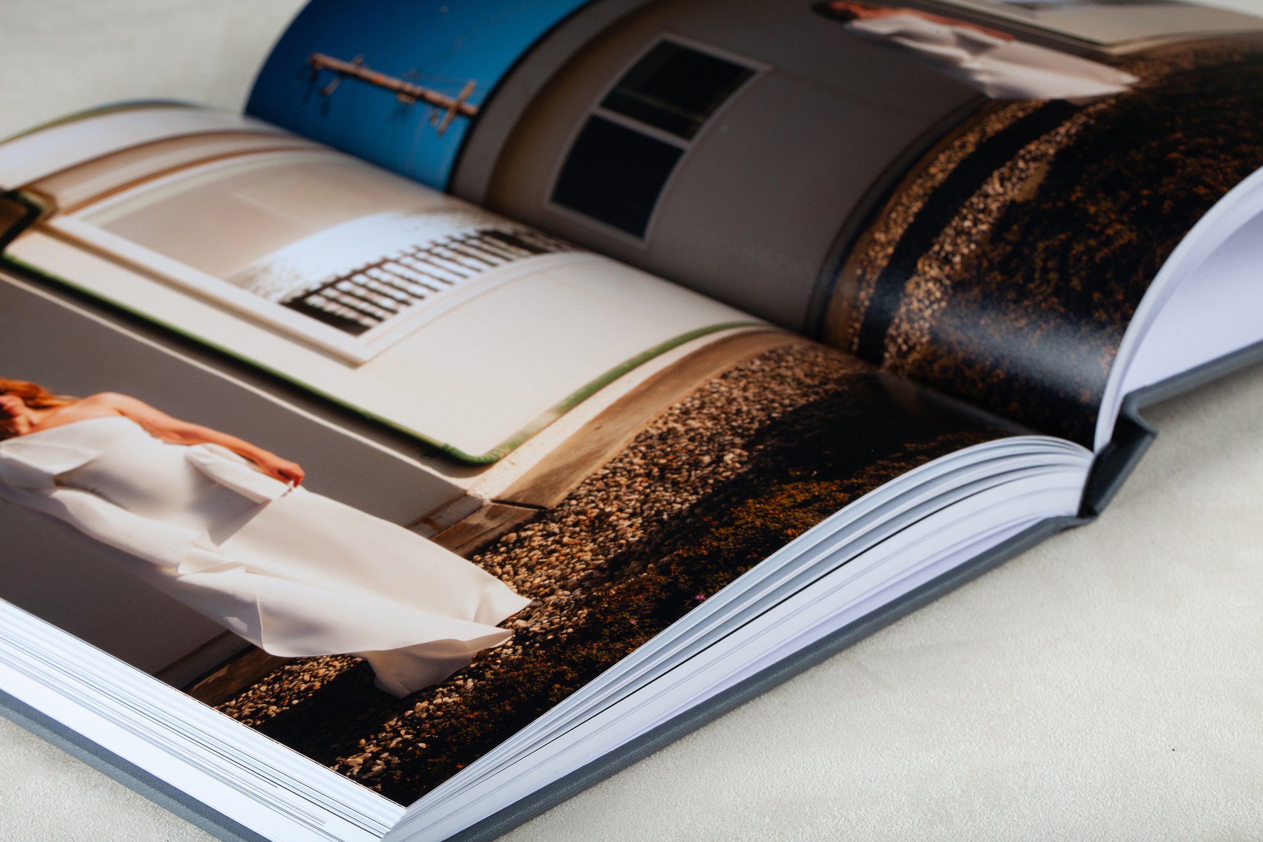 Offene Fotobuchseite mit Bildern von Sand, Wasser und einer Stadtansicht, teilweise bedeckt von Papier.