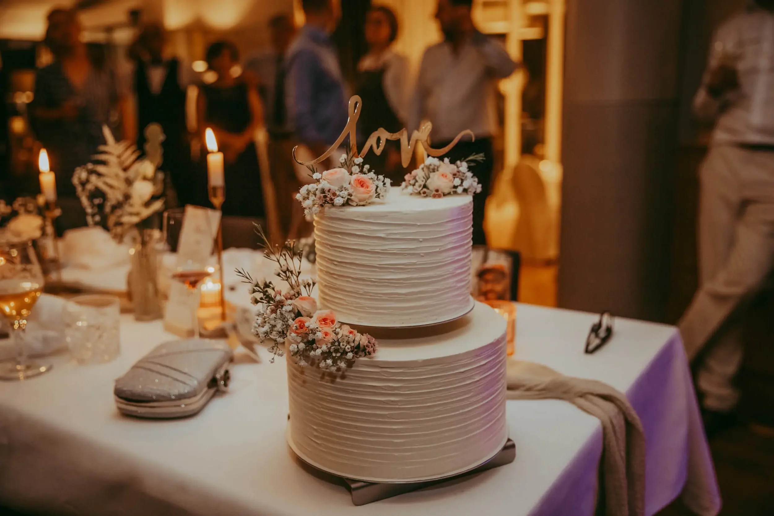 Hochzeitstorte mit Blumen und "love"-Hintergrund in einer festlichen Umgebung mit Kerzen.