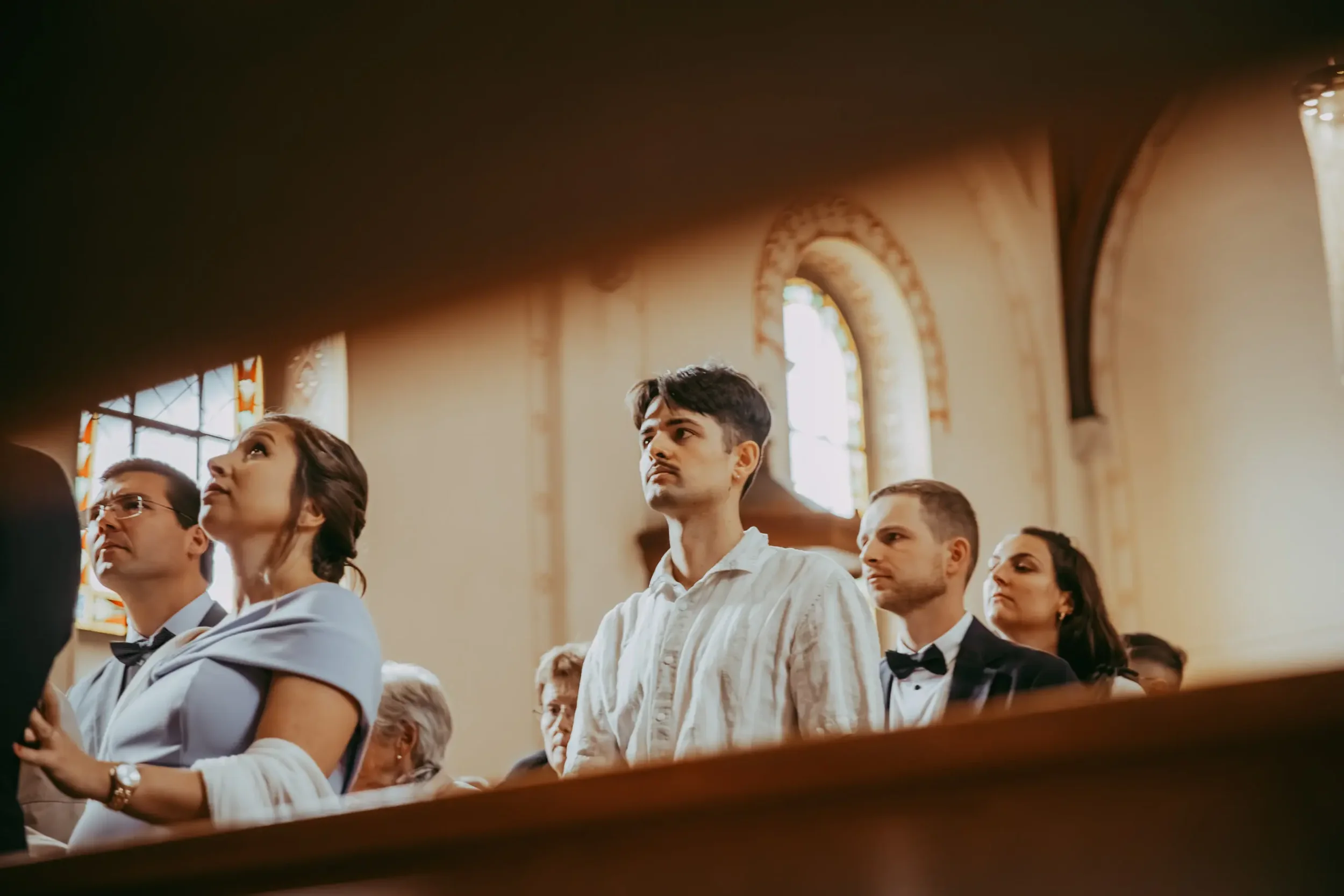 Menschen sitzen im Kirchenraum während einer Zeremonie oder Veranstaltung, mit bunten Fenstern im Hintergrund.
