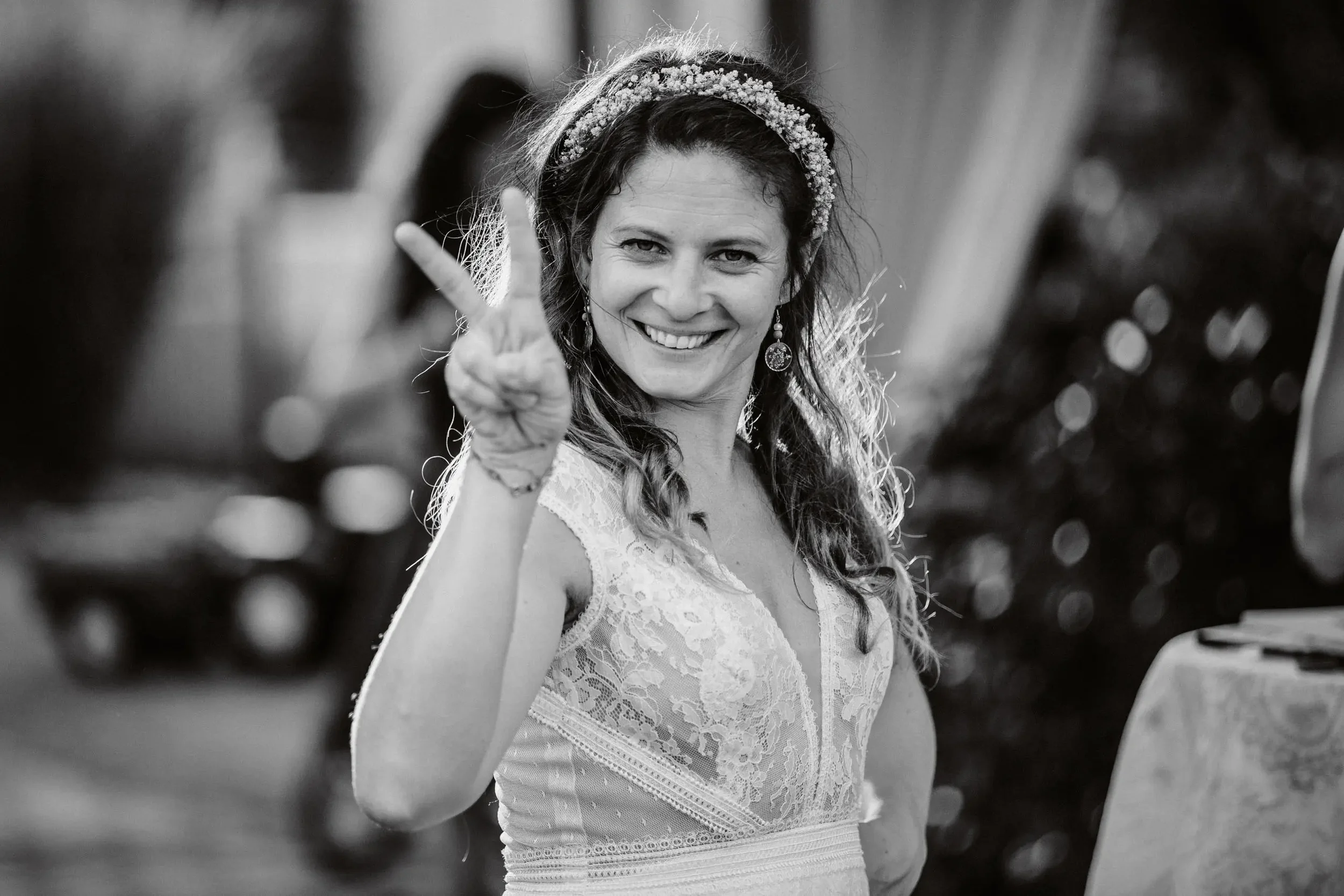 Eine lächelnde Frau in einem weißen Spitzenkleid macht ein Peace-Zeichen mit der Hand.