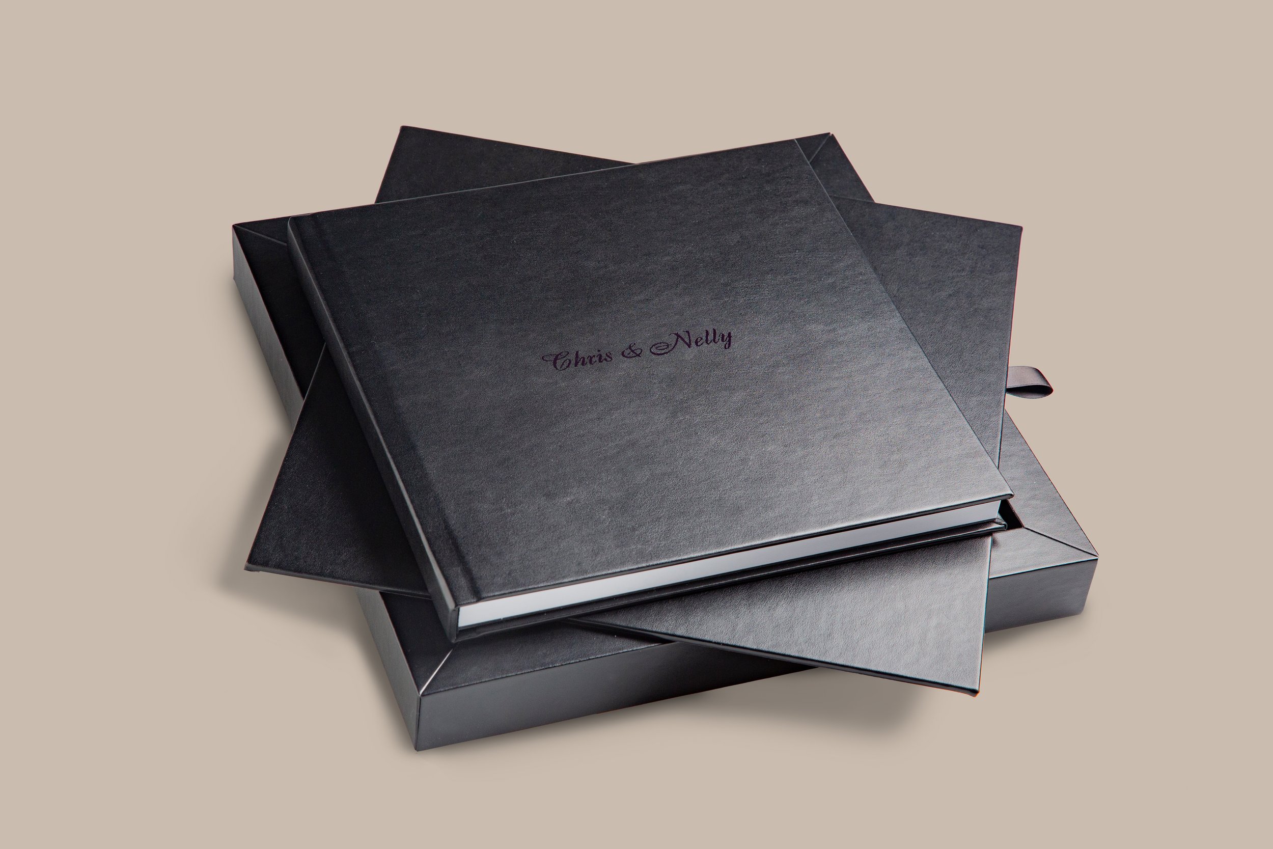 Schwarzes Hochzeitsalbum mit Gravur 'Chris & Nelly' auf einem schwarzen Geschenkkarton, beige Hintergrund.
