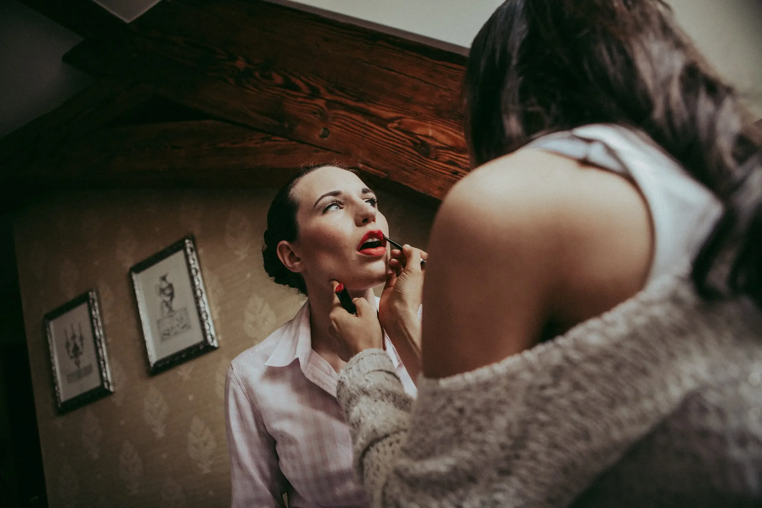 Eine Frau wird von einer anderen Person mit Lippenstift geschminkt. Die Frau trägt ein weißes Hemd.