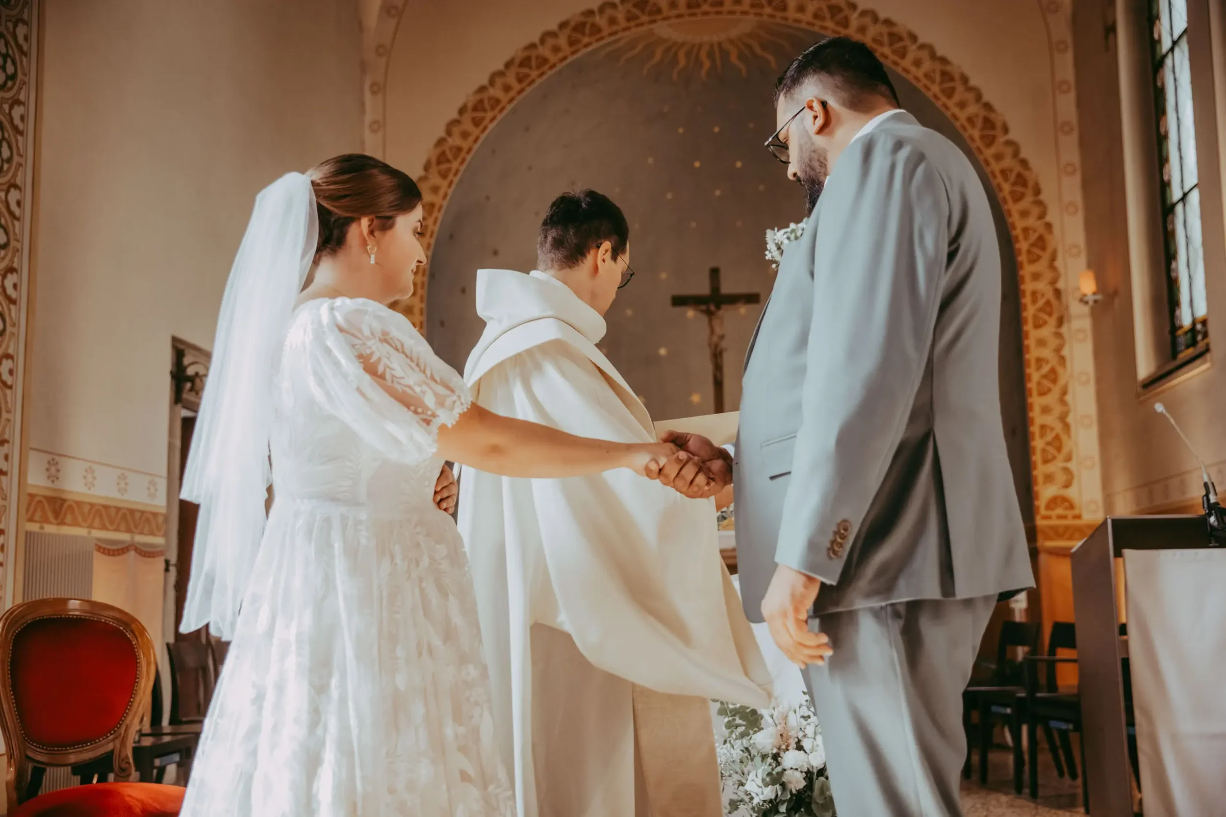 Ein Brautpaar in der Kirche bei der standesamtlichen Trauung, die Hand in Hand vor einem Priester stehen.