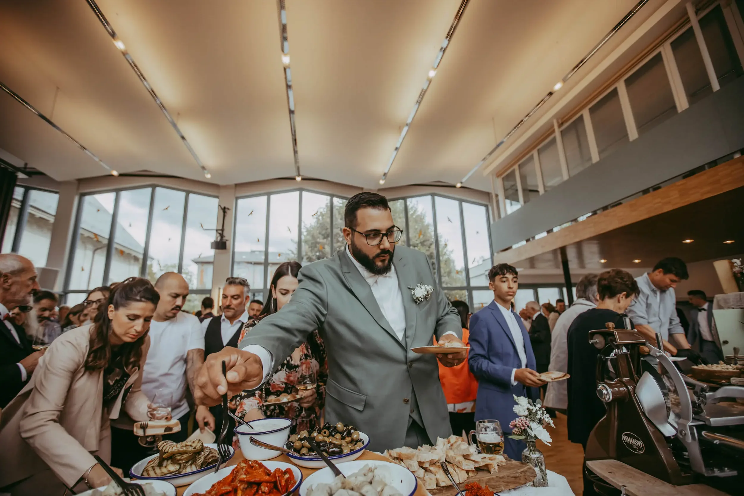 Menschen in einem festlichen Restaurantbuffet, die Essen servieren und genießen, mit großen Fenstern im Hintergrund und moderner Innenarchitektur.