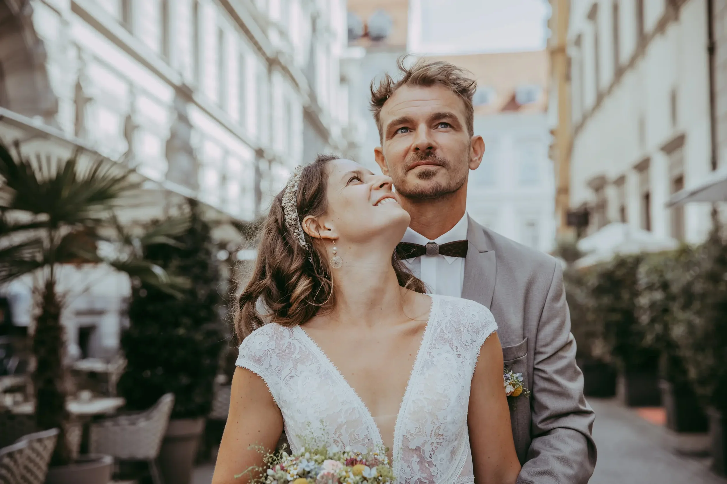 Ein Brautpaar bei einer Hochzeit, die Frau hält einen Blumenstrauß, die Szene ist in einem Gebäude mit viel natürlichem Licht.
