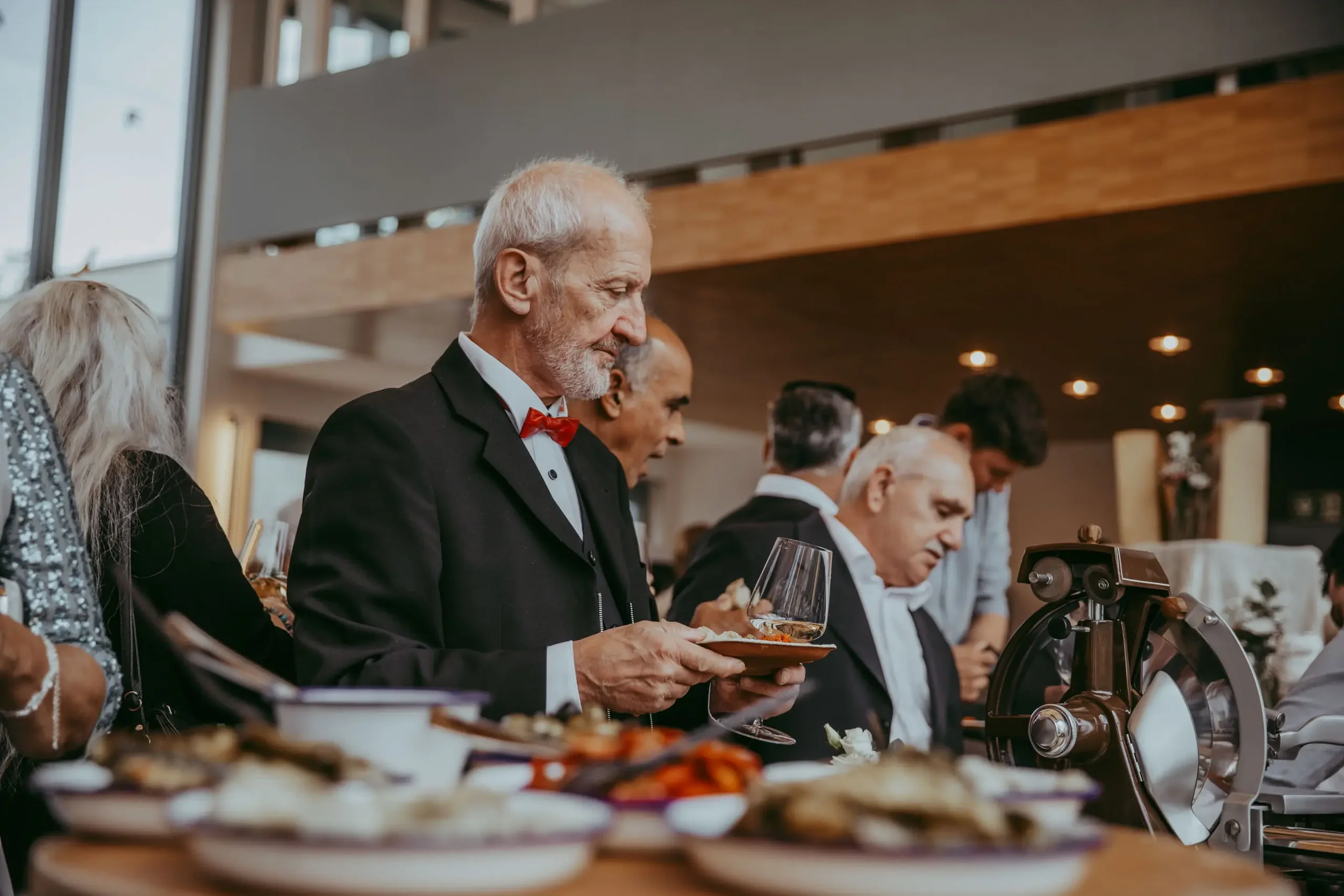 Älterer Mann mit grauem Bart und roter Fliege beim Essen in einem Restaurant.