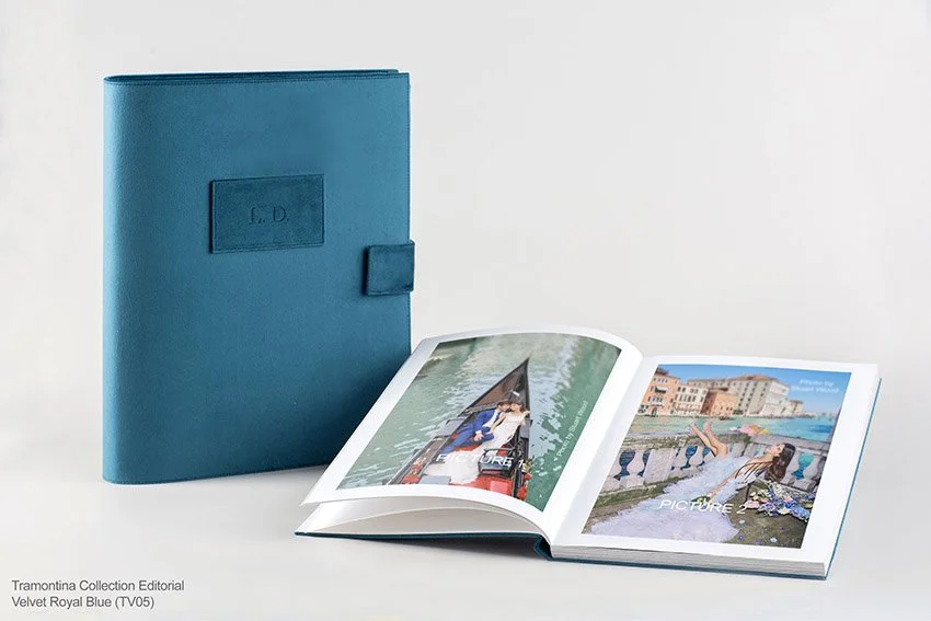 Ein offenes Fotobuch mit Urlaubsfotos neben einem blauen Ordner auf weißem Hintergrund.