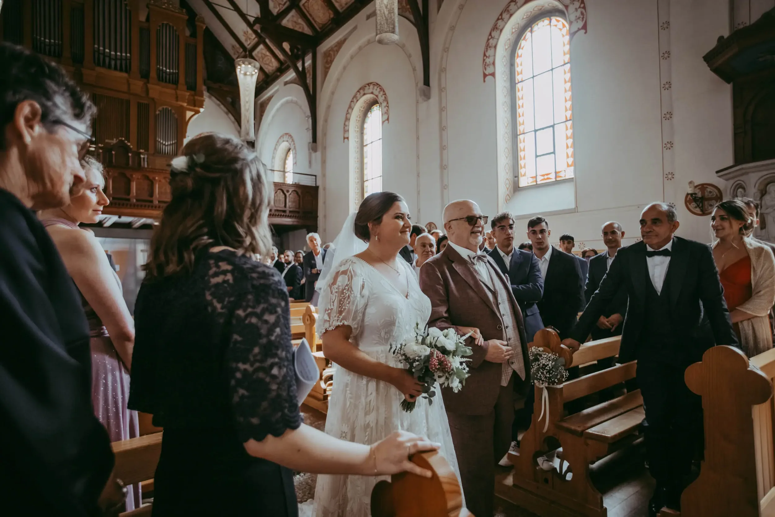 Hochzeit in einer Kirche mit Braut, Brautpaar, Hochzeitsgästen und Kirchenarchitektur im Hintergrund.