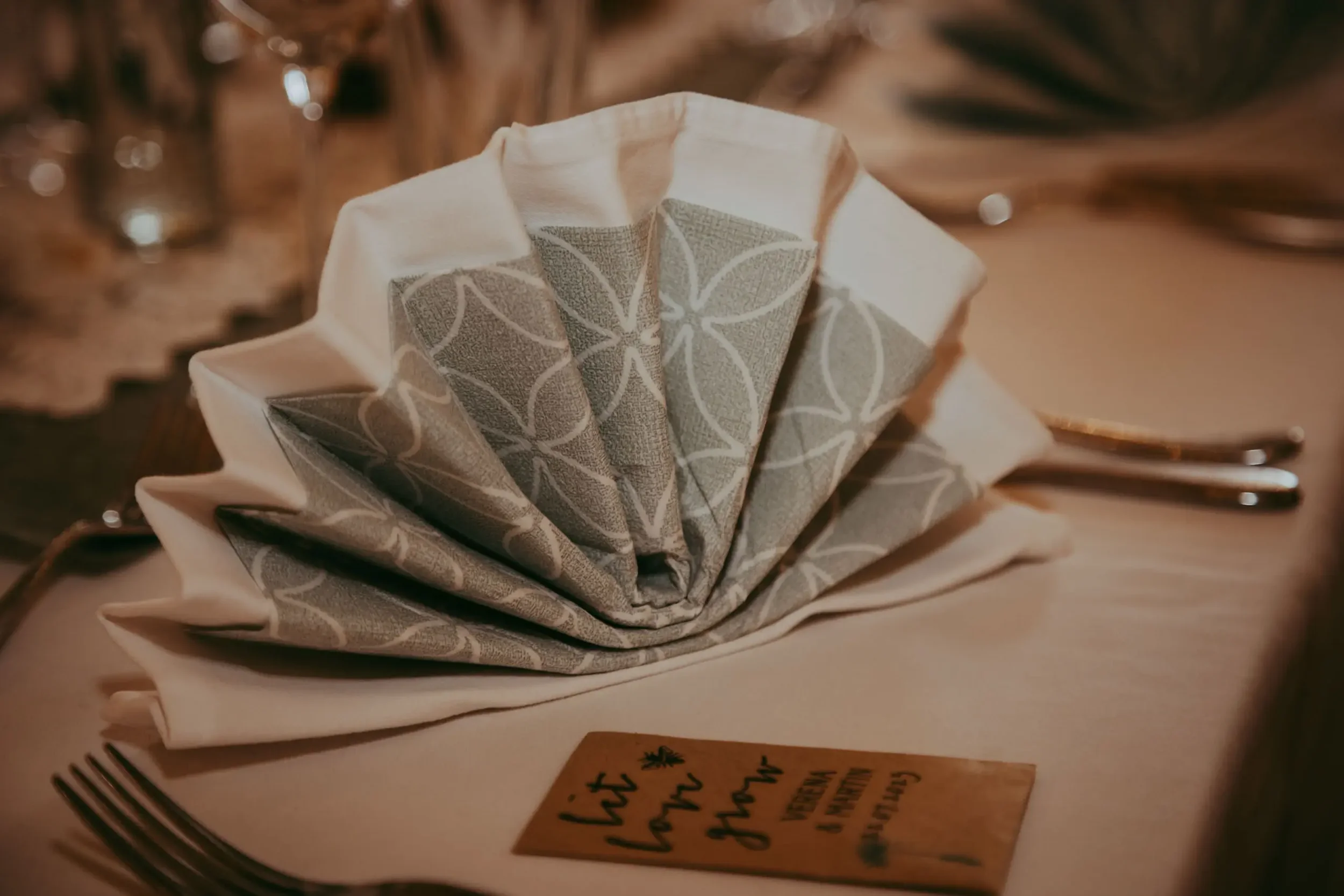 Ein bestickter Stoffteller in der Mitte eines Tisches, umgeben von Besteck und Papptellern, vermutlich für ein Buffet oder eine Feier.