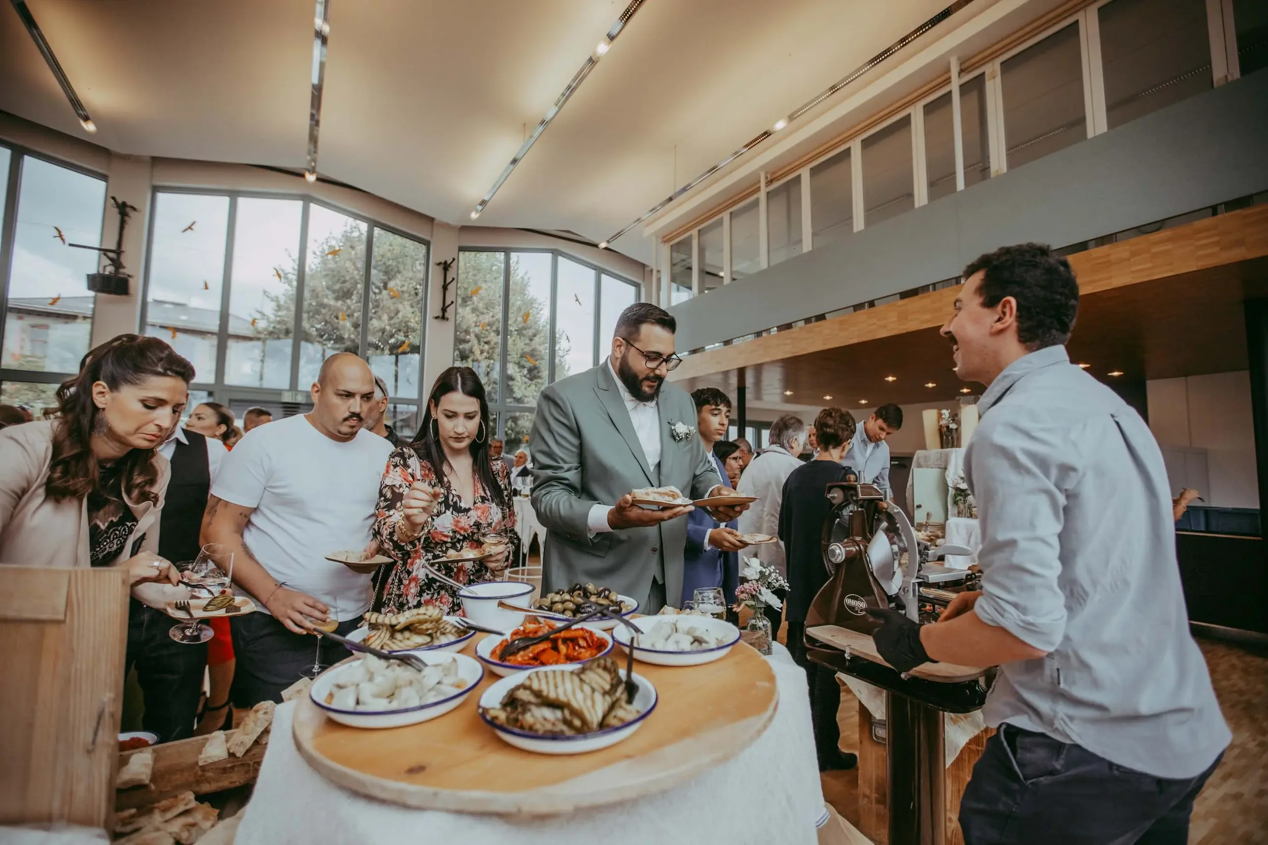 Menschen in einem modernen Speisesaal beim Essen und Zahlen, dabei steht eine Servicekraft hinter einem Verkaufsstand mit verschiedenen Speisen.