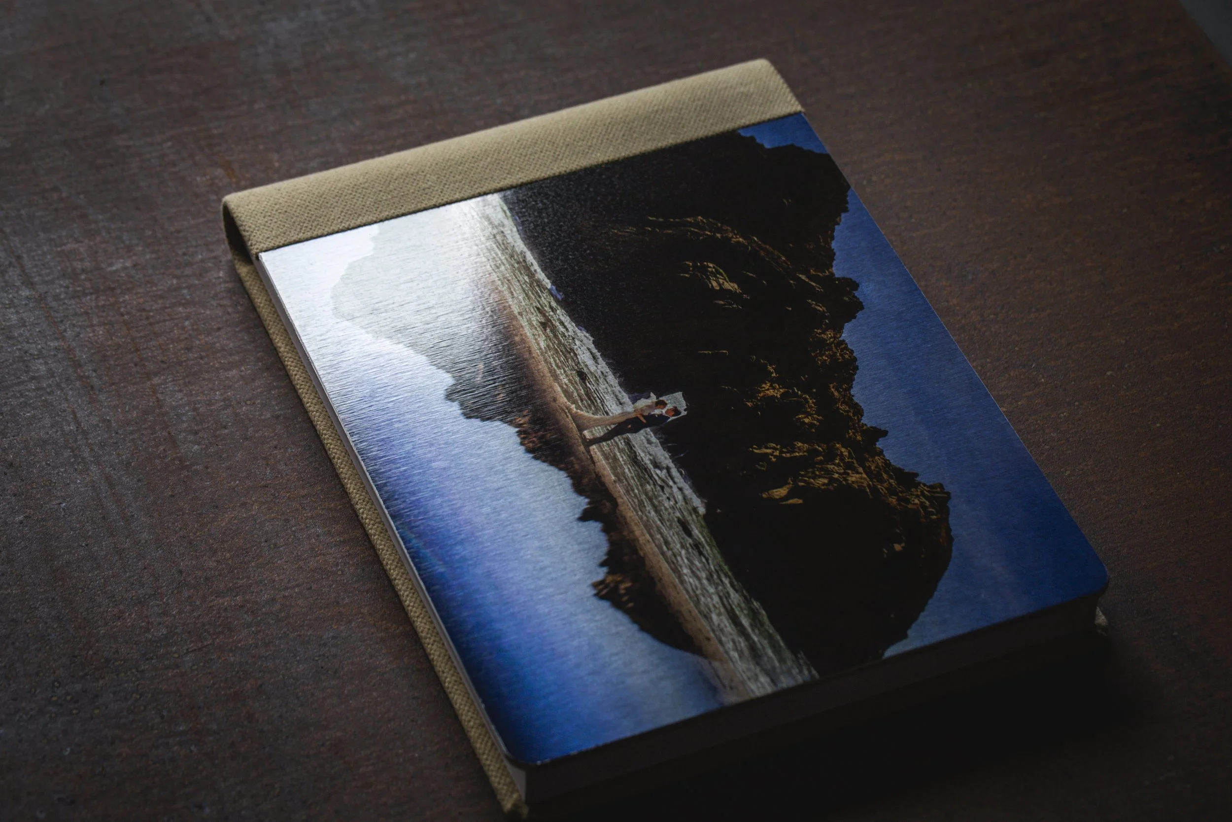 Fotobuch mit Landschaftsbild von einem Fluss, Strand und Felsen, liegend auf einem dunklen Holztisch.