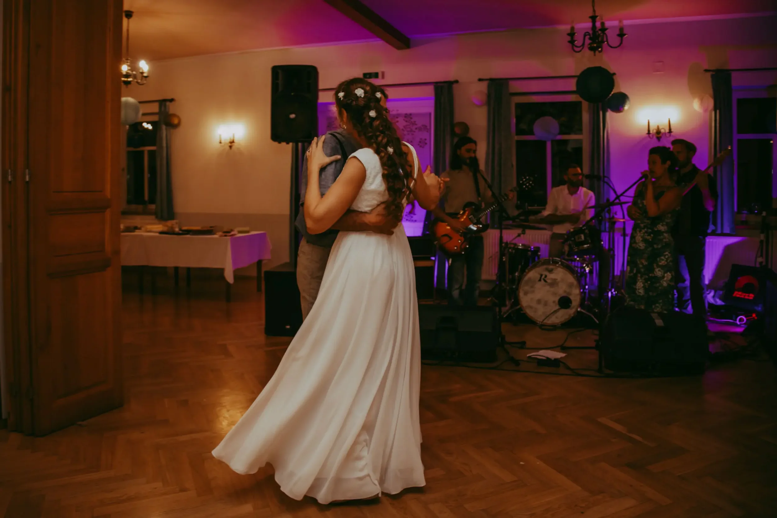 Ein Hochzeitspaar tanzt in einem festlich dekorierten Veranstaltungsraum mit Musikband im Hintergrund.