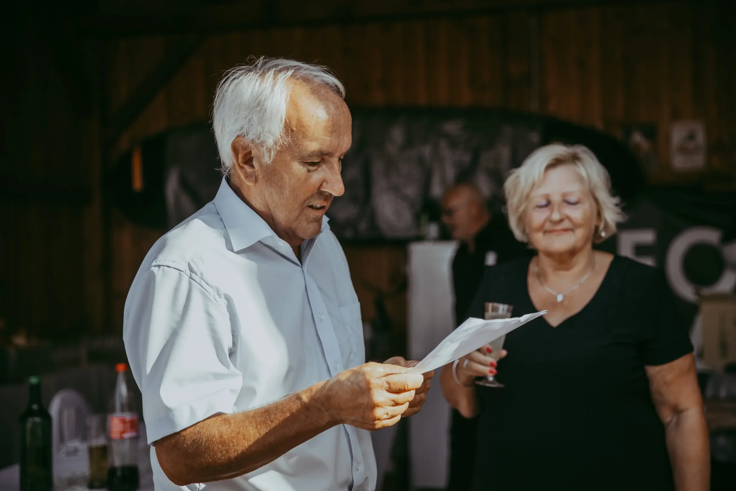 Älterer Mann liest eine Speisekarte in einem Restaurant, neben einer älteren Frau, die ein Weinglas hält.