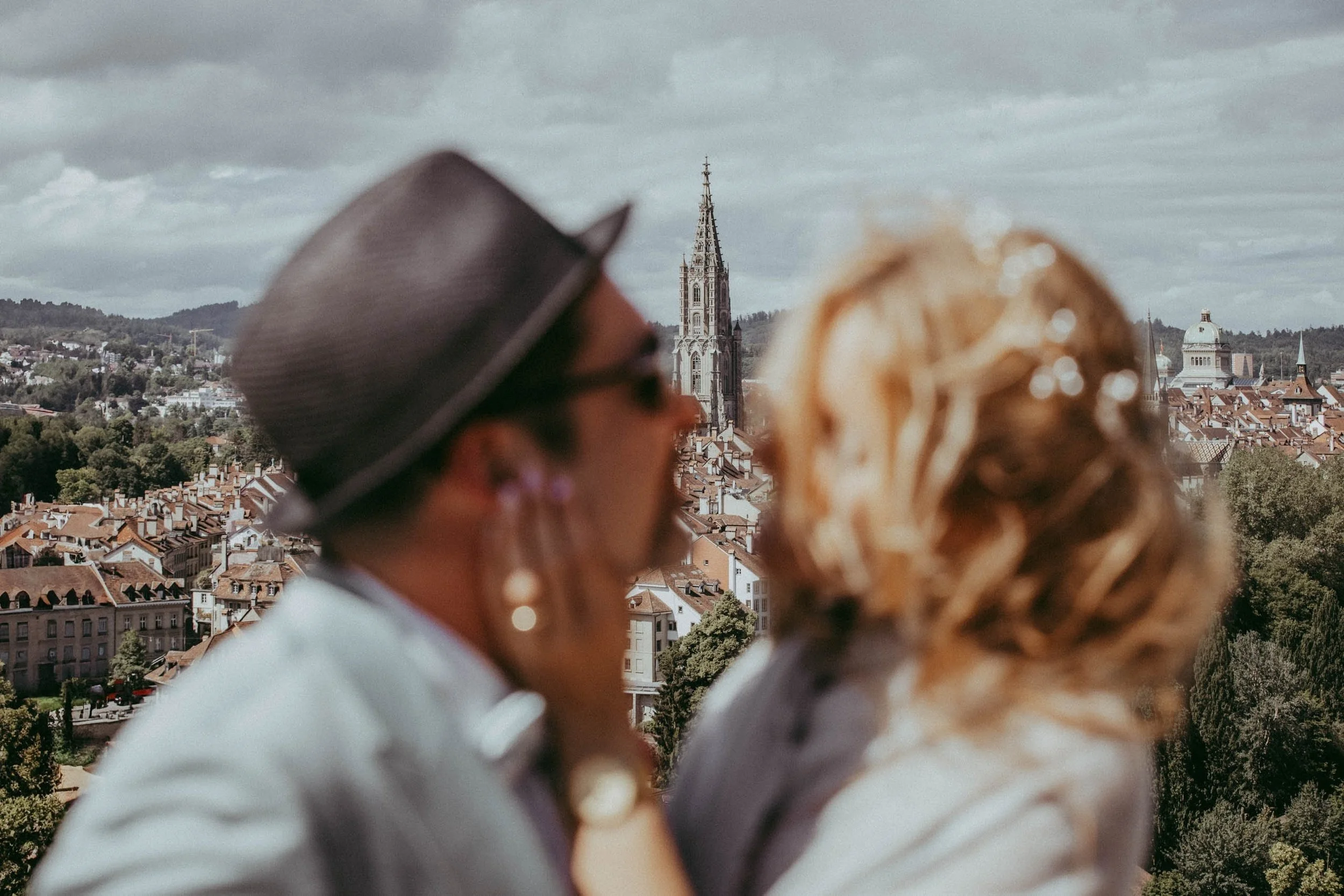 Menschen beim Blick auf eine Stadt mit einem gotischen Kirchturm im Hintergrund, leicht verschwommen im Vordergrund.