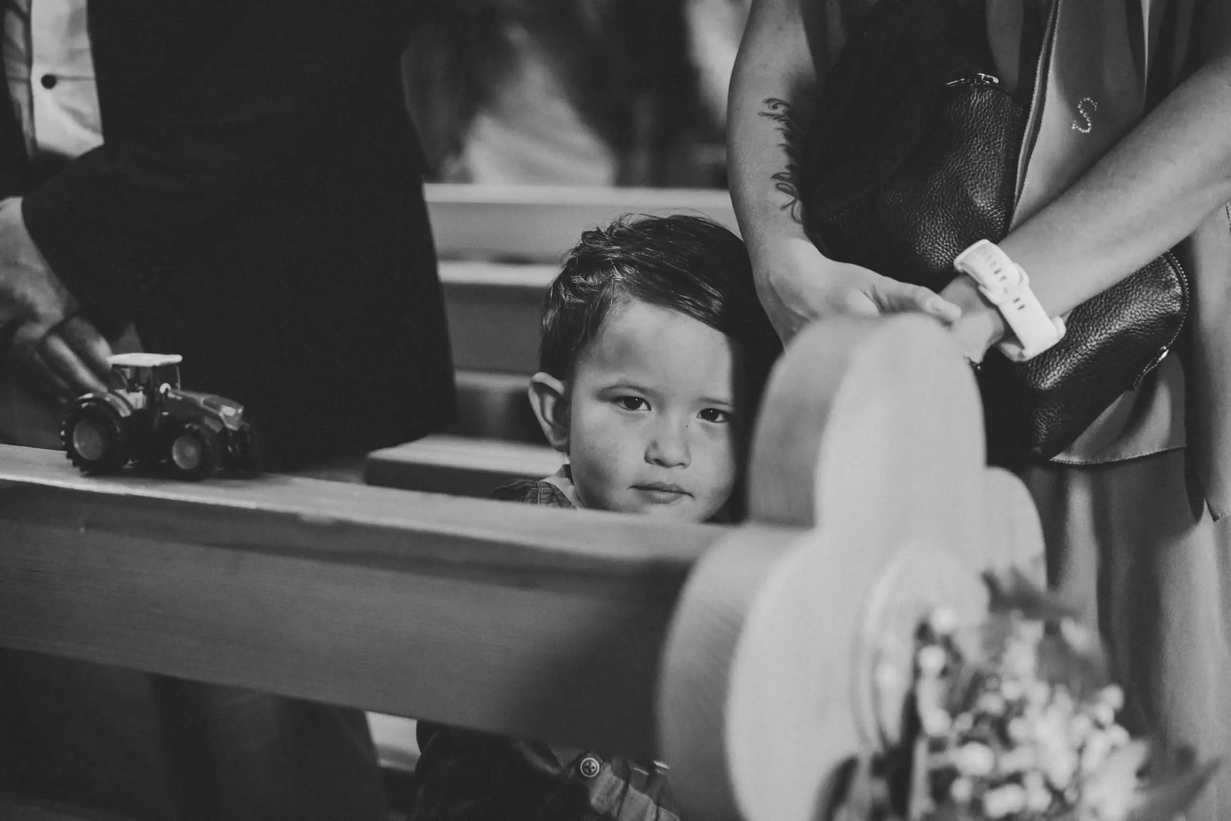 Ein Junge schaut durch eine Öffnung in einer Spielstruktur, während eine Frau über ihm lehnt. Es scheint eine Spielhalle oder ein Indoor-Spielplatz zu sein, mit Spielzeug auf der Tischplatte im Vordergrund.