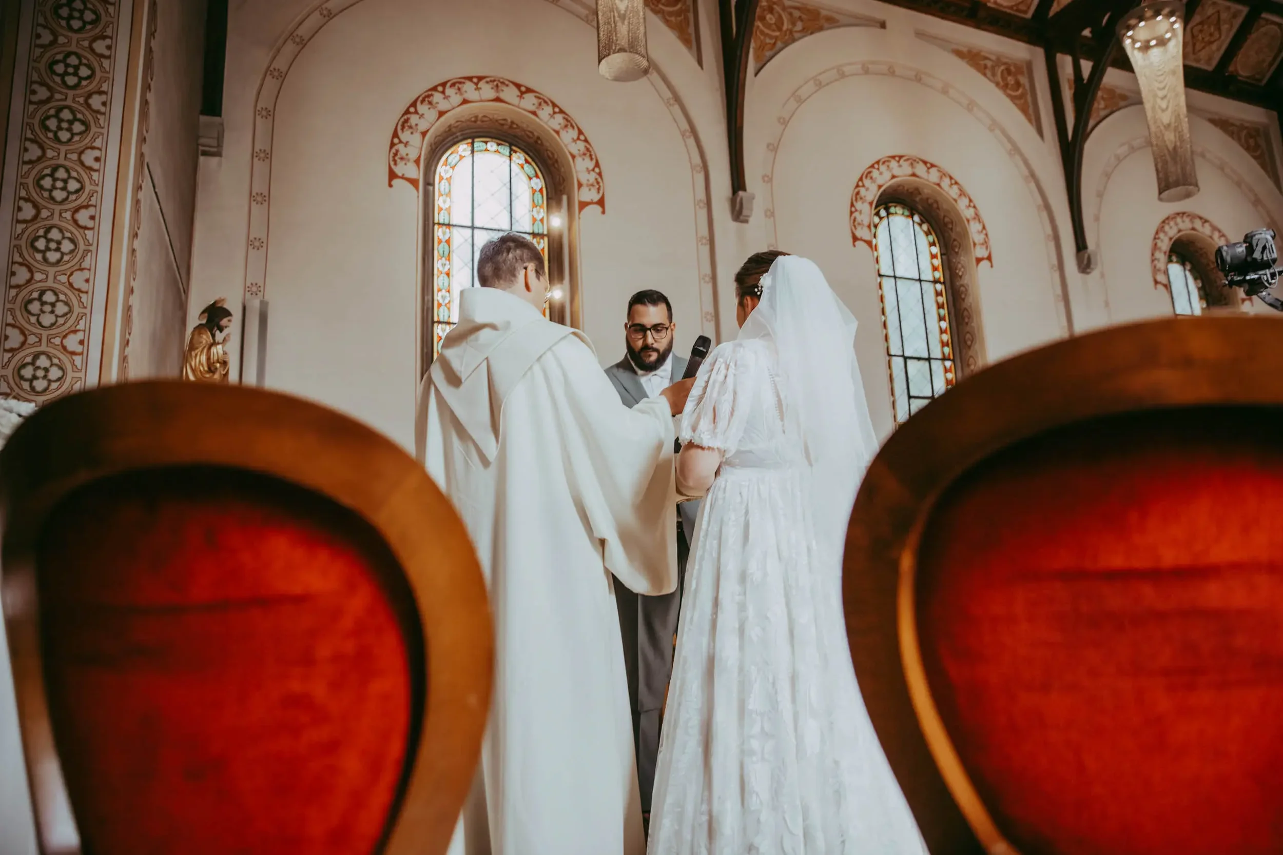 Zwei Menschen bei einer Hochzeit, die in einer Kirche vor einem Priester stehen, während das Paar einander das Eheversprechen gibt.