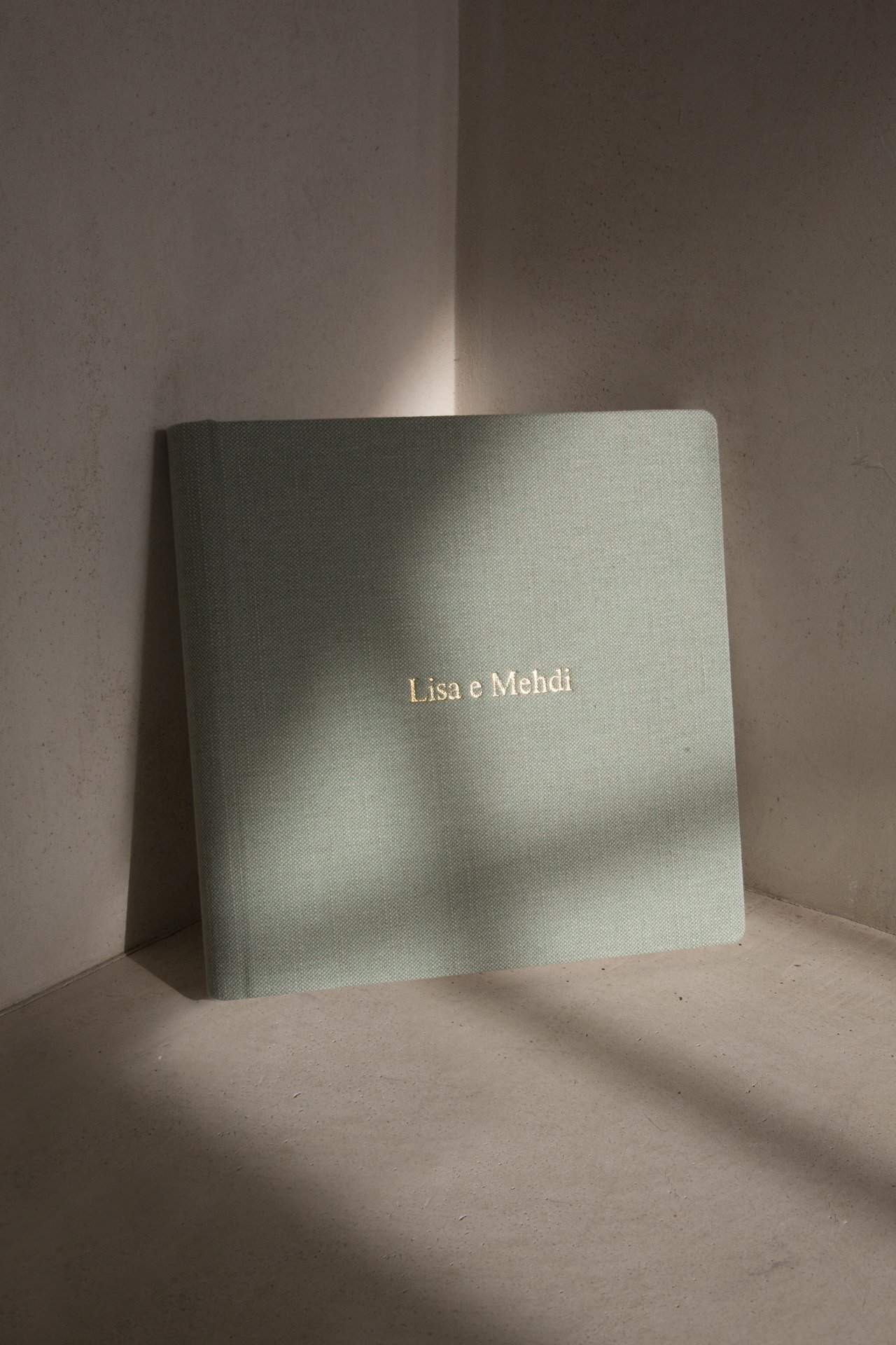 Ein grünes Buch mit goldenem Buchstaben, auf dem steht: 『Lisa e Mehdi』, steht auf einem hellen, glatten Untergrund in einer Ecke.